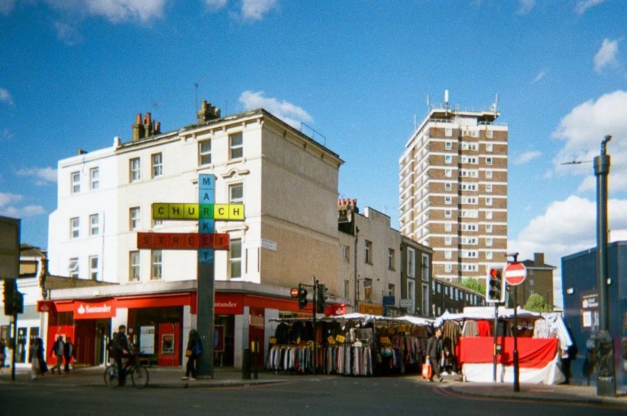 Street scene with a street market, a Santander bank branch, and colorful street signs in London, England.