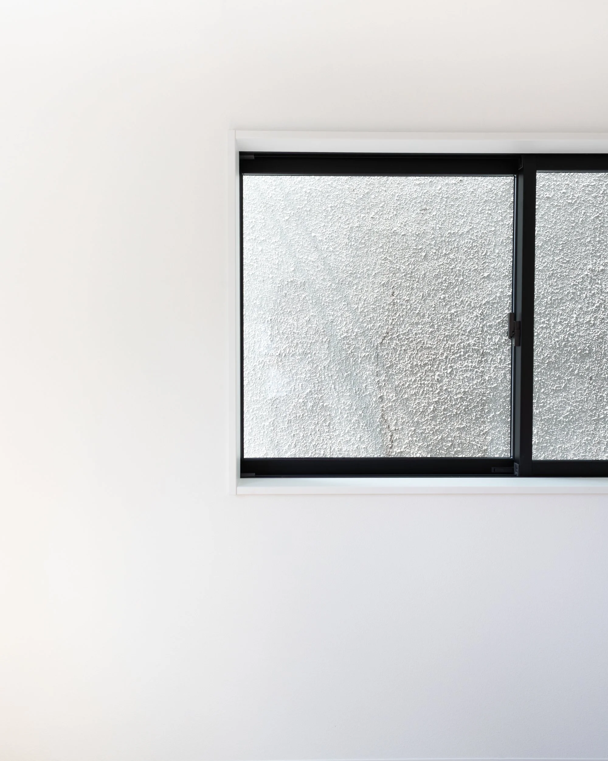 A window with black frame on a white wall, showing frosted glass.