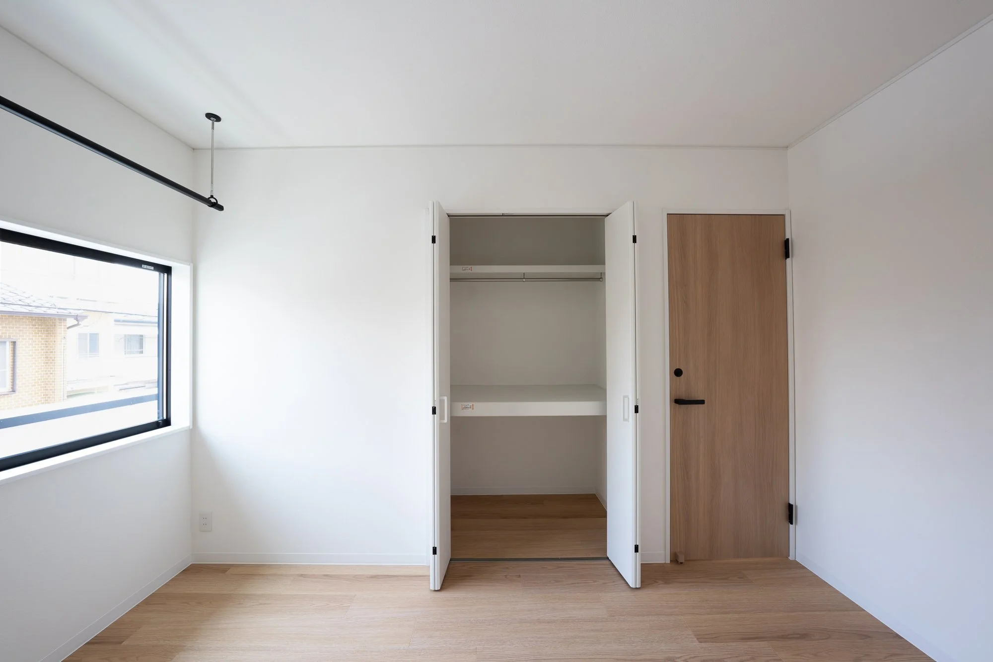 Empty room with a window, white walls, a closet with open doors, and a wooden door.