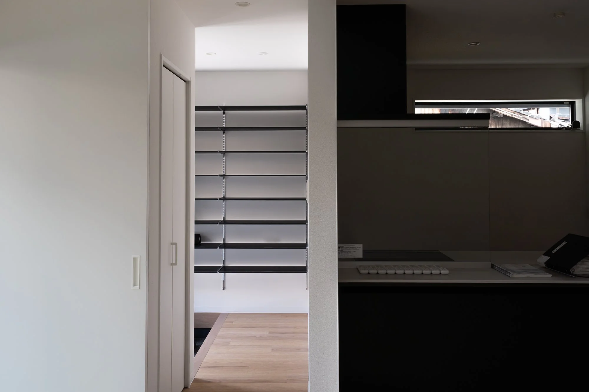 Interior view of a modern home, showing a white sliding door, a mostly empty black bookshelf, hardwood floors, and a small window in the background.