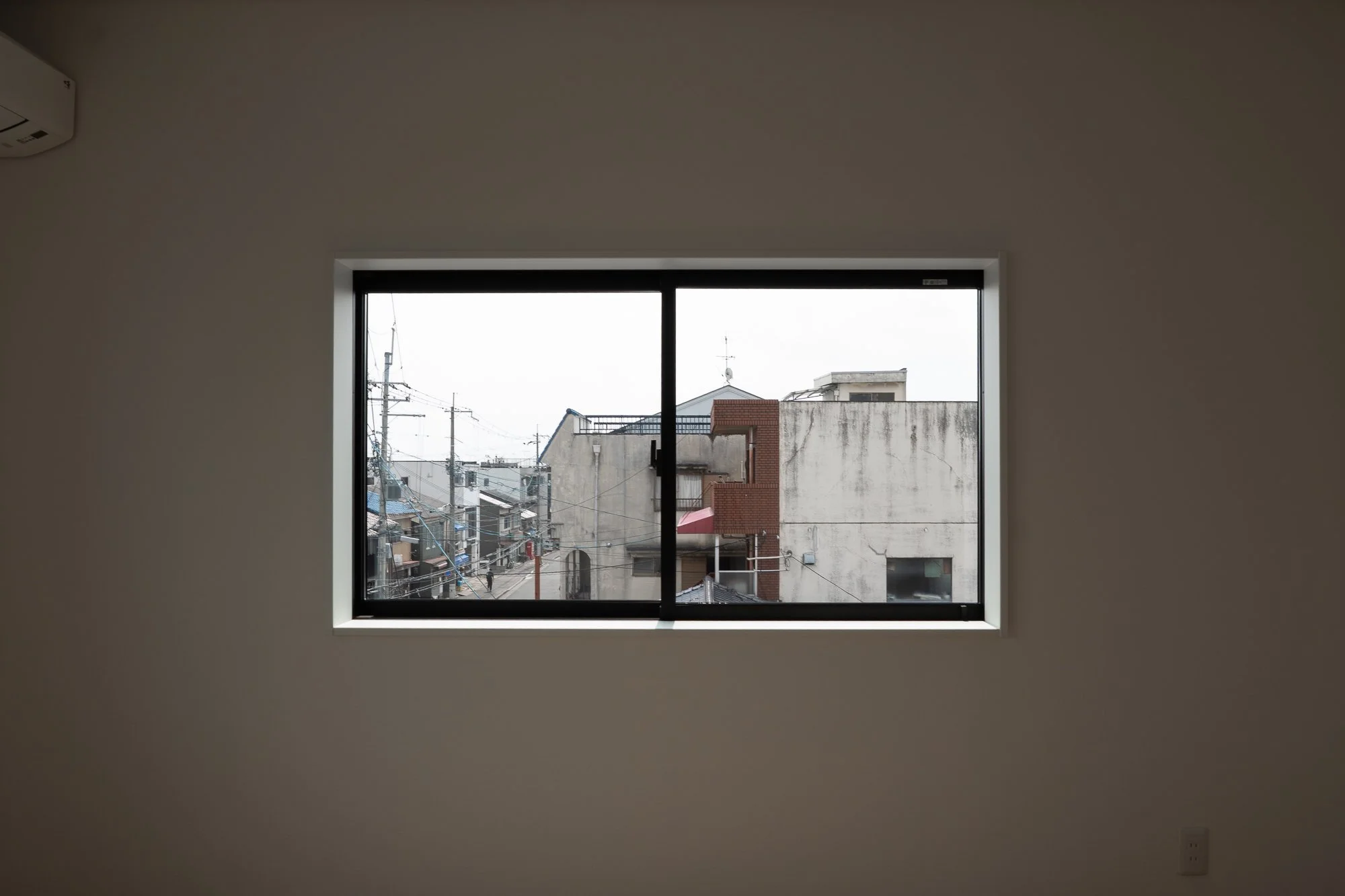 View of urban buildings through a rectangular window with black frame, set in a plain white wall.