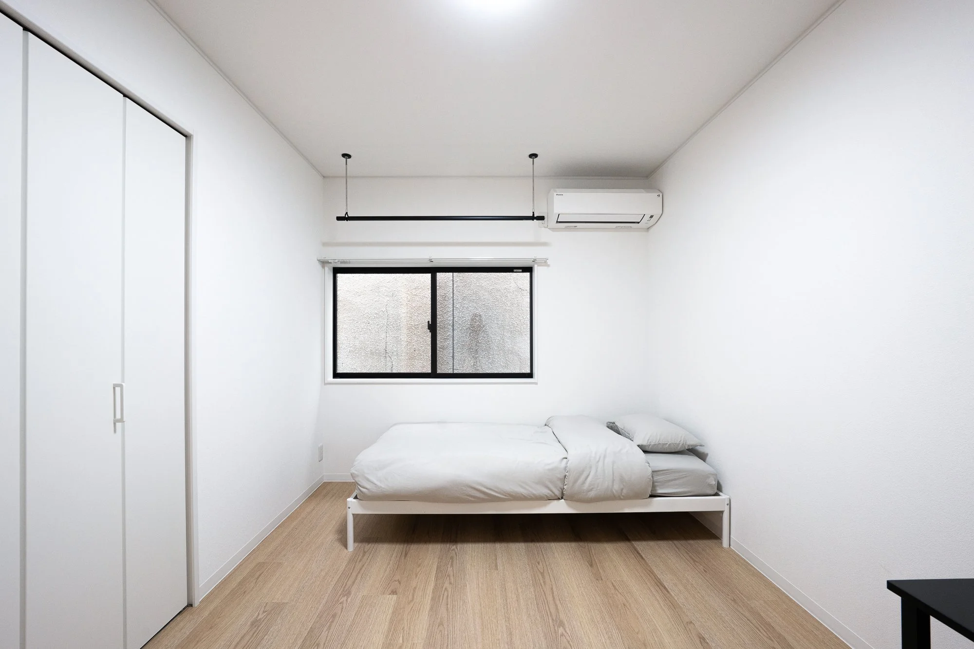 Simple, minimally furnished white bedroom with a bed, window, closet, and air conditioning unit.