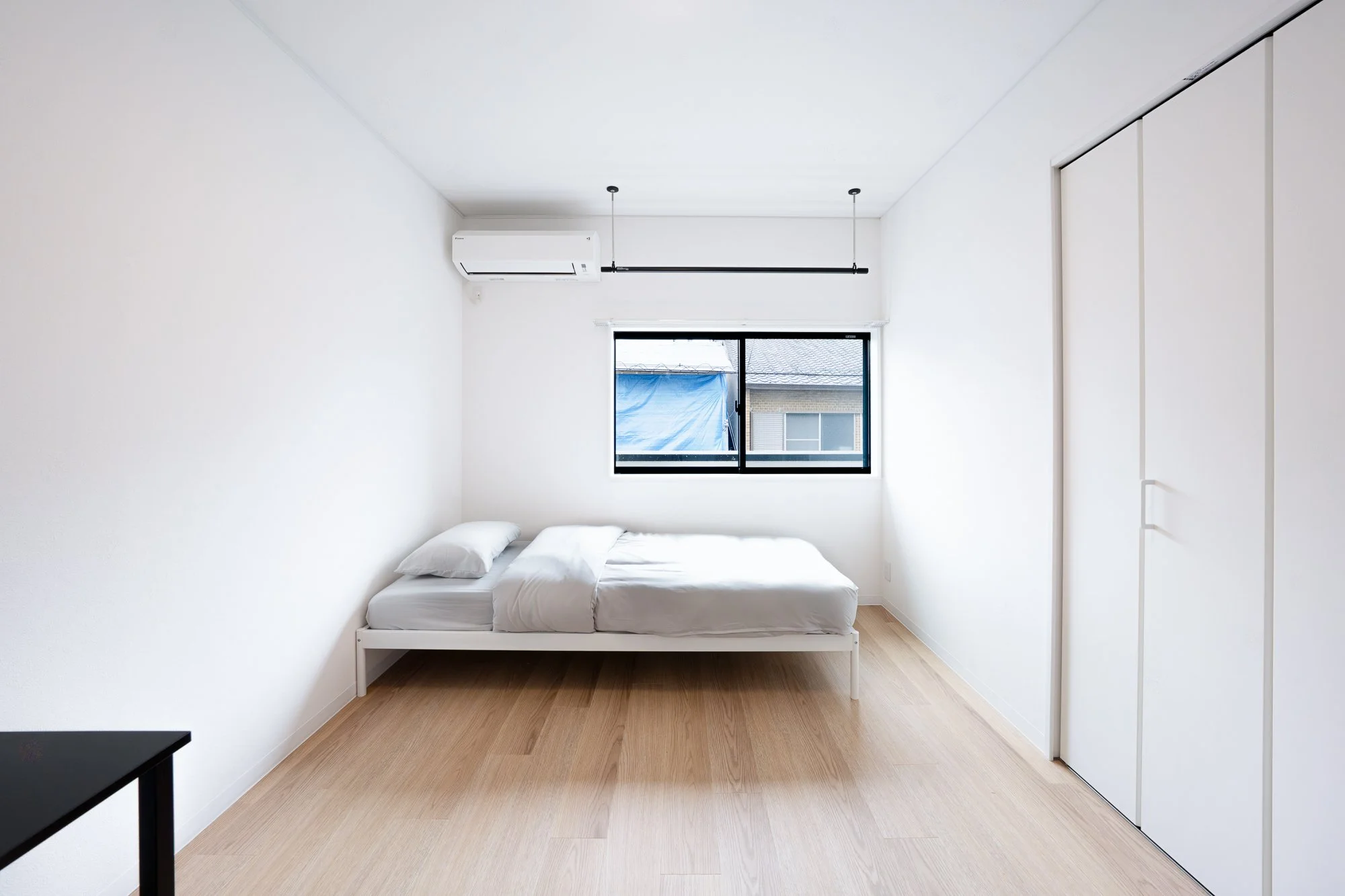 Minimalist bedroom with a white bed, white walls, hardwood floor, a window, and a closet with sliding doors.