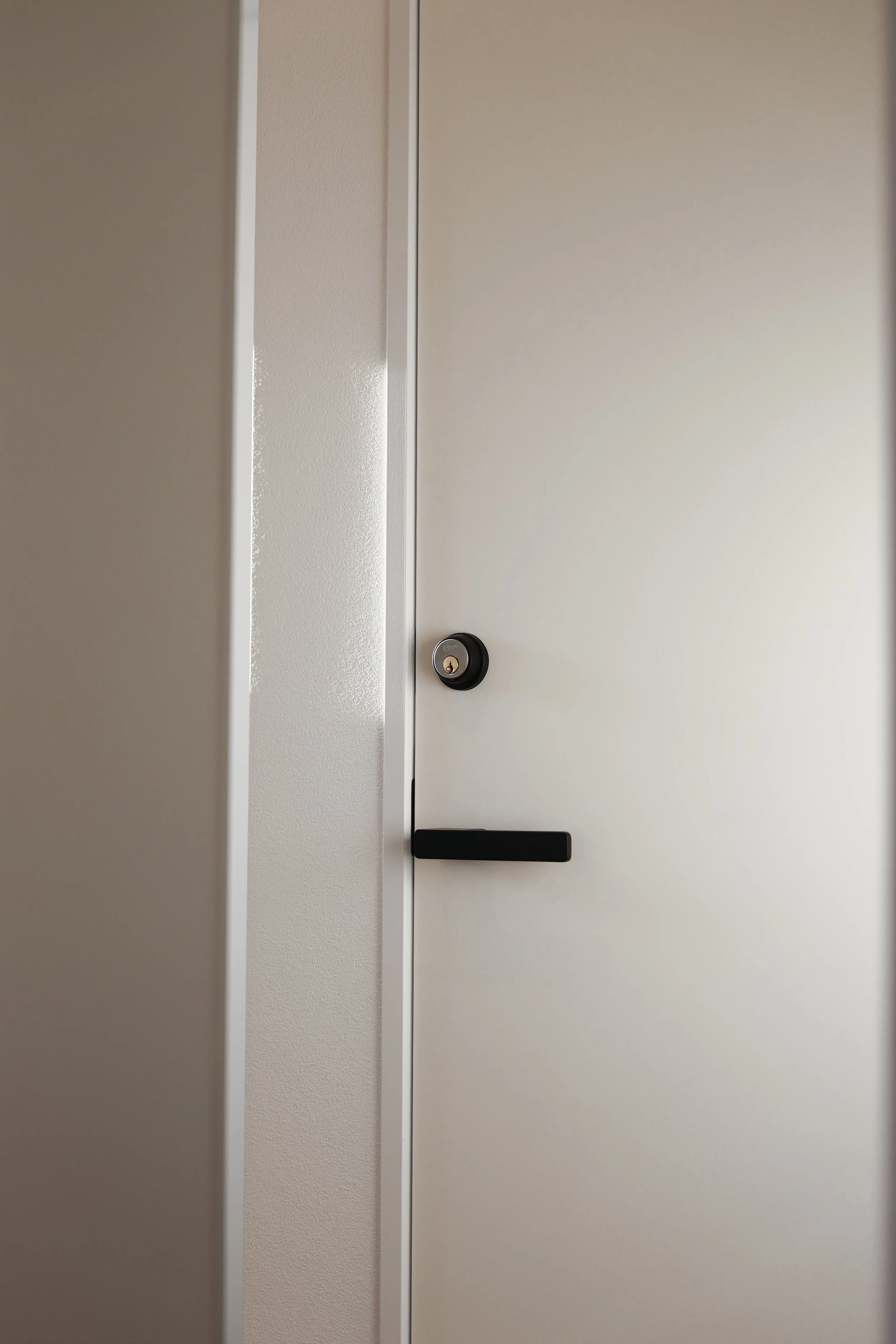 Close-up of a white door with a black handle and a round lock, partially open, revealing a white wall.