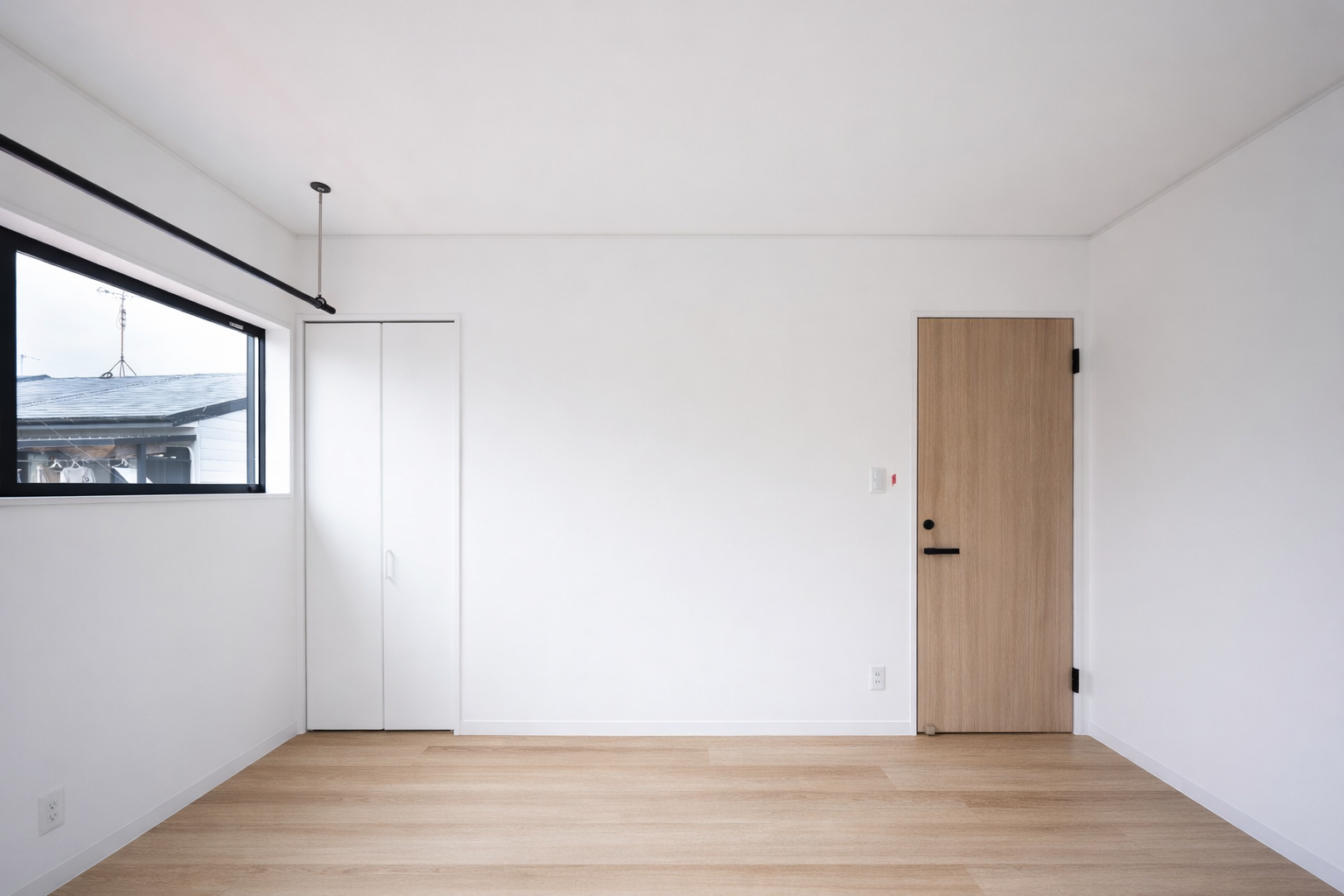 Empty room with white walls, a window on the left, a small door closet, and a wooden door on the right.