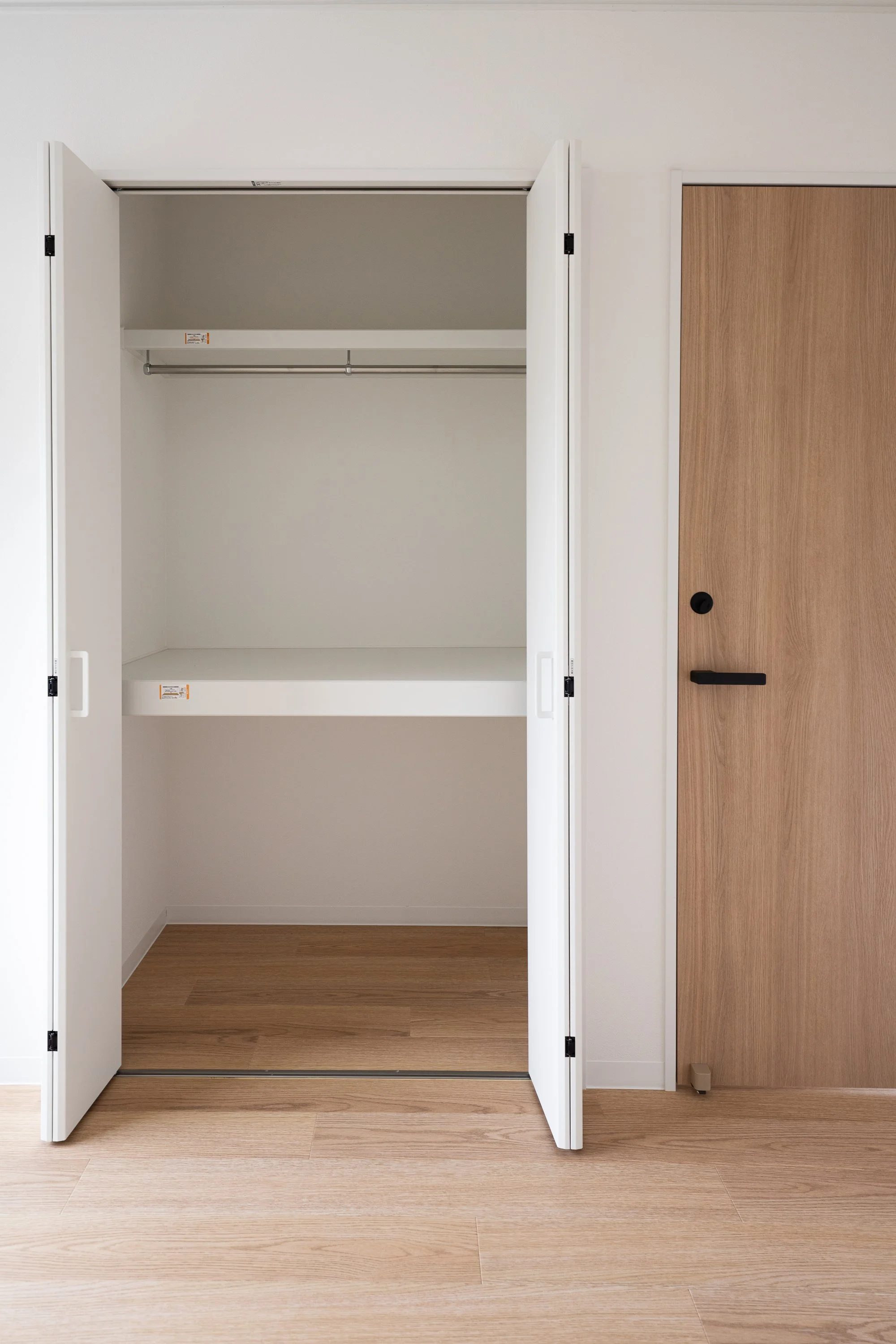 Empty closet with white sliding doors and a clothing rod, next to a wood-colored door.
