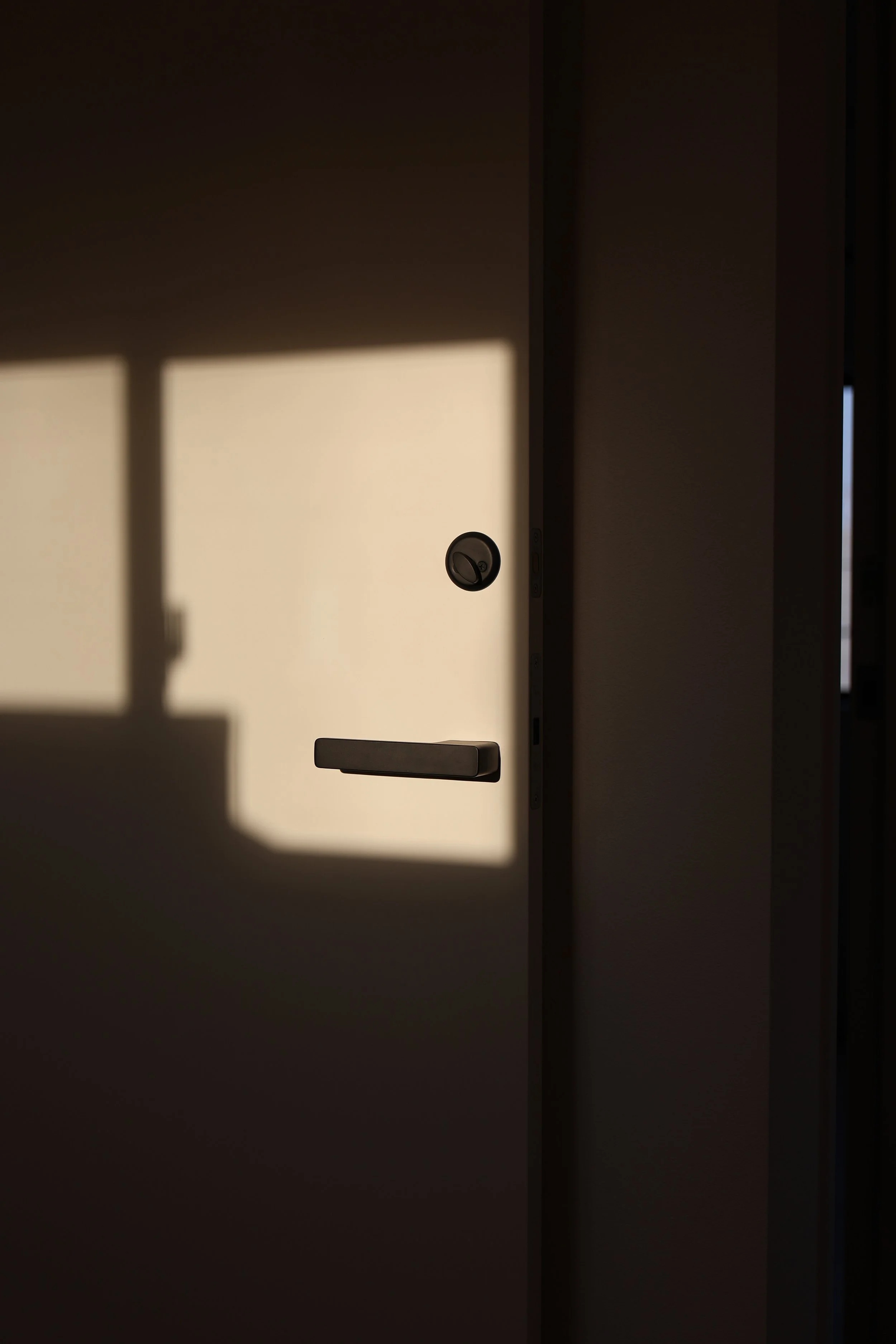 A door partially open with sunlight casting a shadow of the window frame onto it.