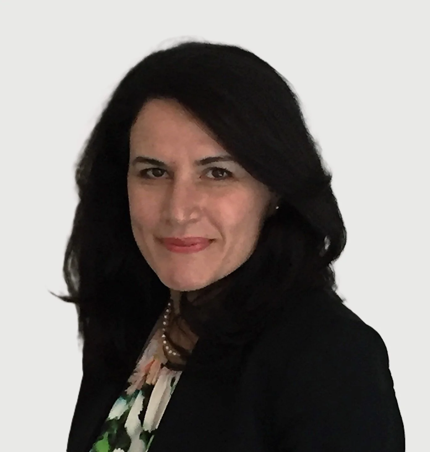 A woman with black hair, wearing a floral dress, pearl necklace, and black blazer, smiling against a plain white background.
