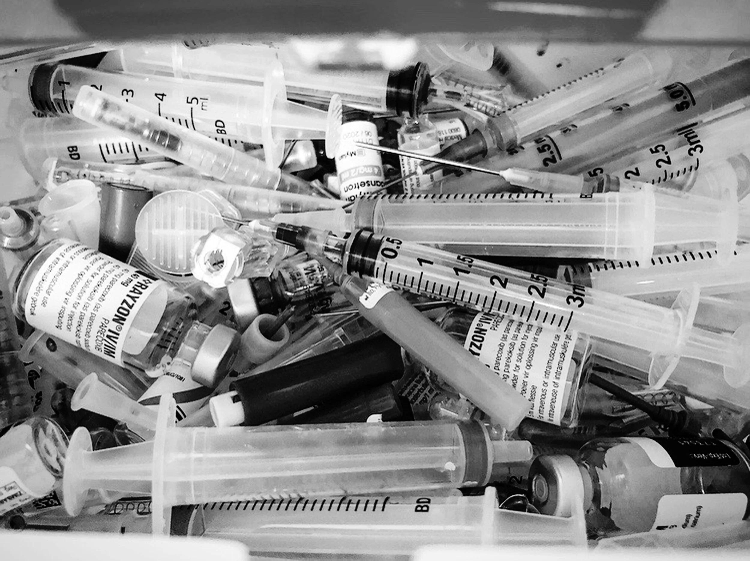 A collection of syringes and medication vials in a plastic container.