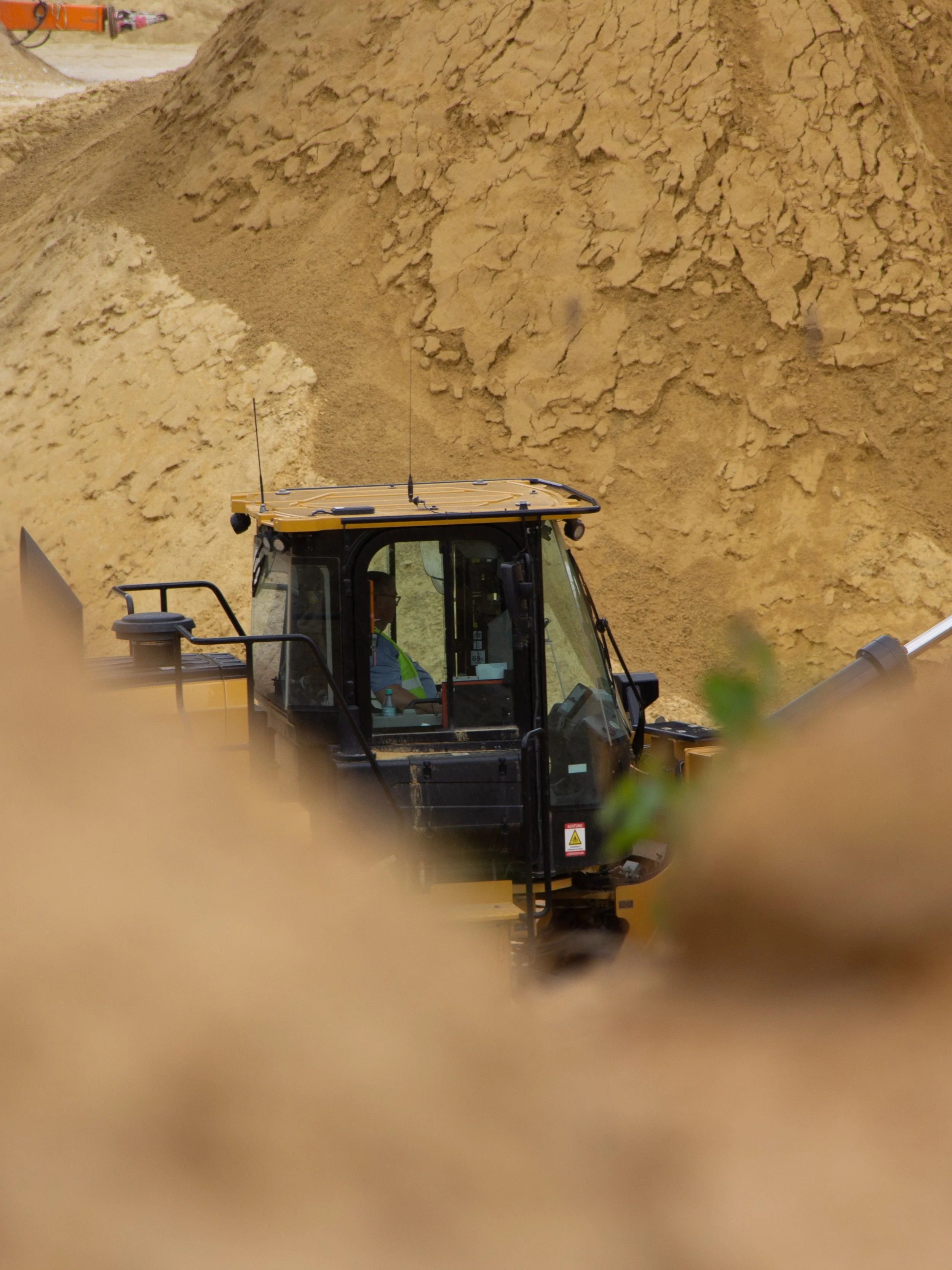 Blick auf einen Bagger bei der Arbeit im Baugebiet, im Hintergrund eine Erdrückenschicht.