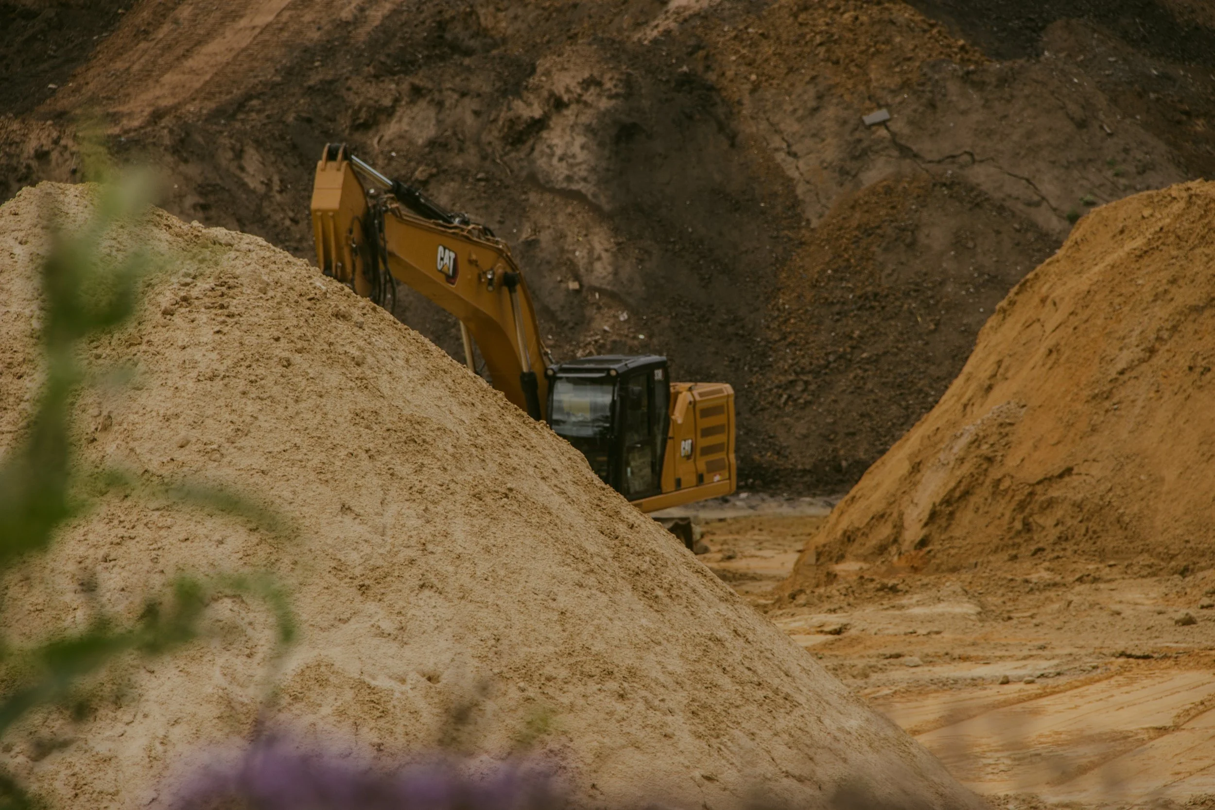 Ein Bagger arbeitet auf einer Sandgrube und bewegt Erde in einer ländlichen Gegend.