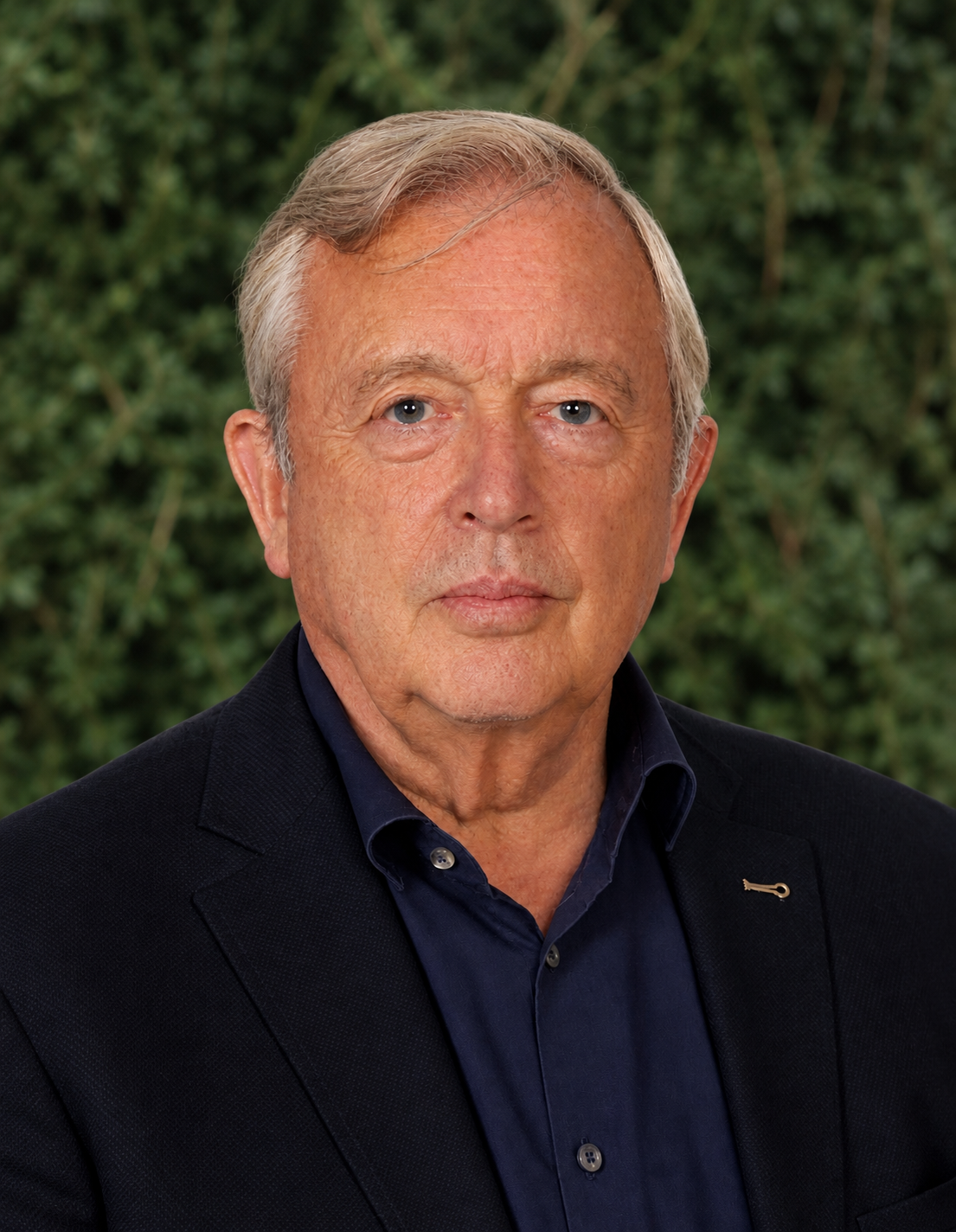 Alter Mann in Geschäftsanzug vor grünem Busch. Nahaufnahme, focus auf Gesicht und Oberkörper.