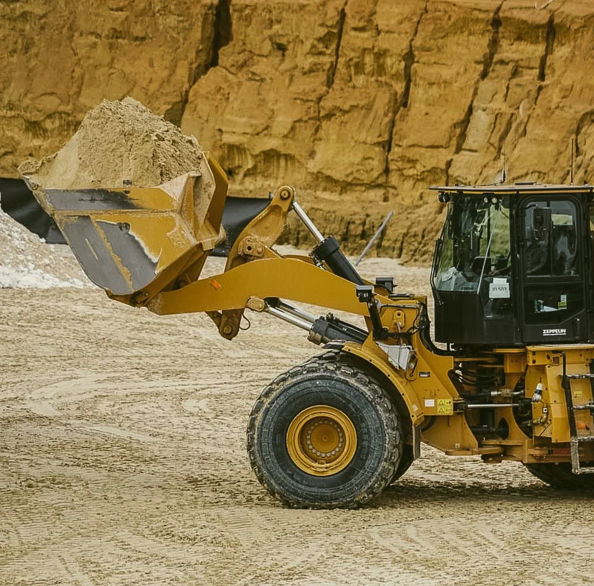 Bagger bei der Arbeit auf einer Sandbaustelle vor einer Felswand.