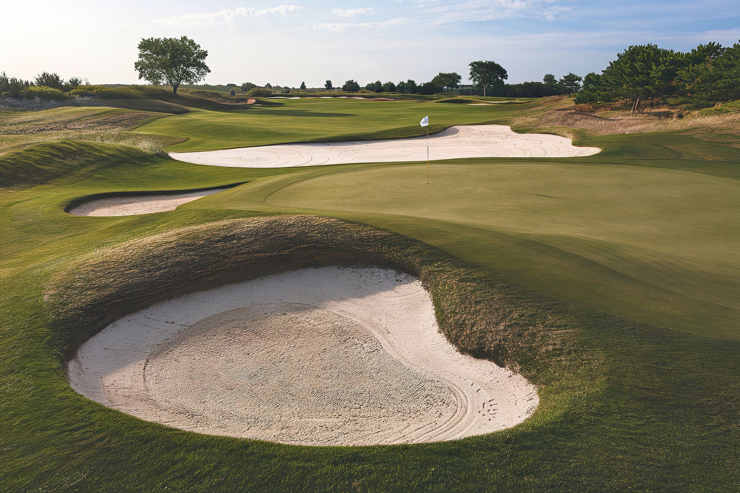 Golfplatz mit Grüns, Bunker und Flagge, umgeben von Bäumen und Natur.