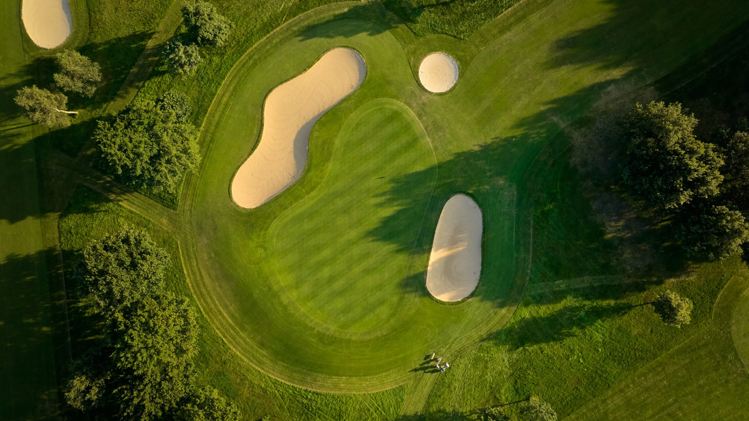 Luftaufnahme eines Golfplatzes mit mehreren Sandbunkern und umgeben von Bäumen.
