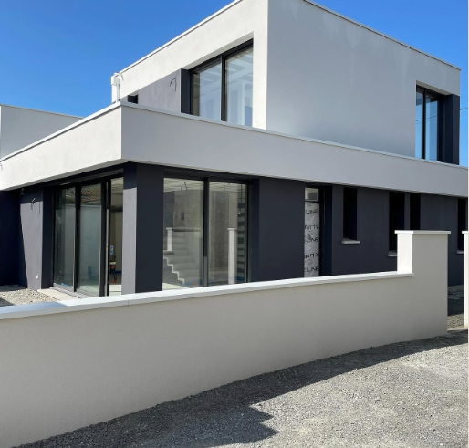 Blanc mat en façade, gris anthracite sur les menuiseries. La peinture extérieure travaille autant que l'architecture.