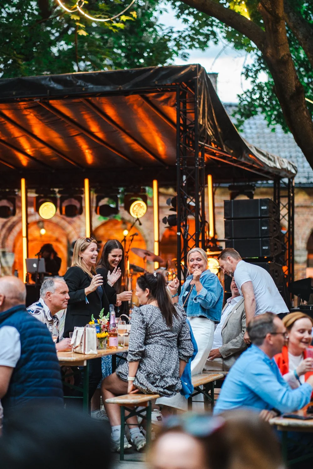 Mennesker som samles og har det gøy utendørs under en konsert i uteområdet Kirkeristen Vertshus bak Domkirken midt i Oslo Sentrum, med et opplyst scenen i bakgrunnen.