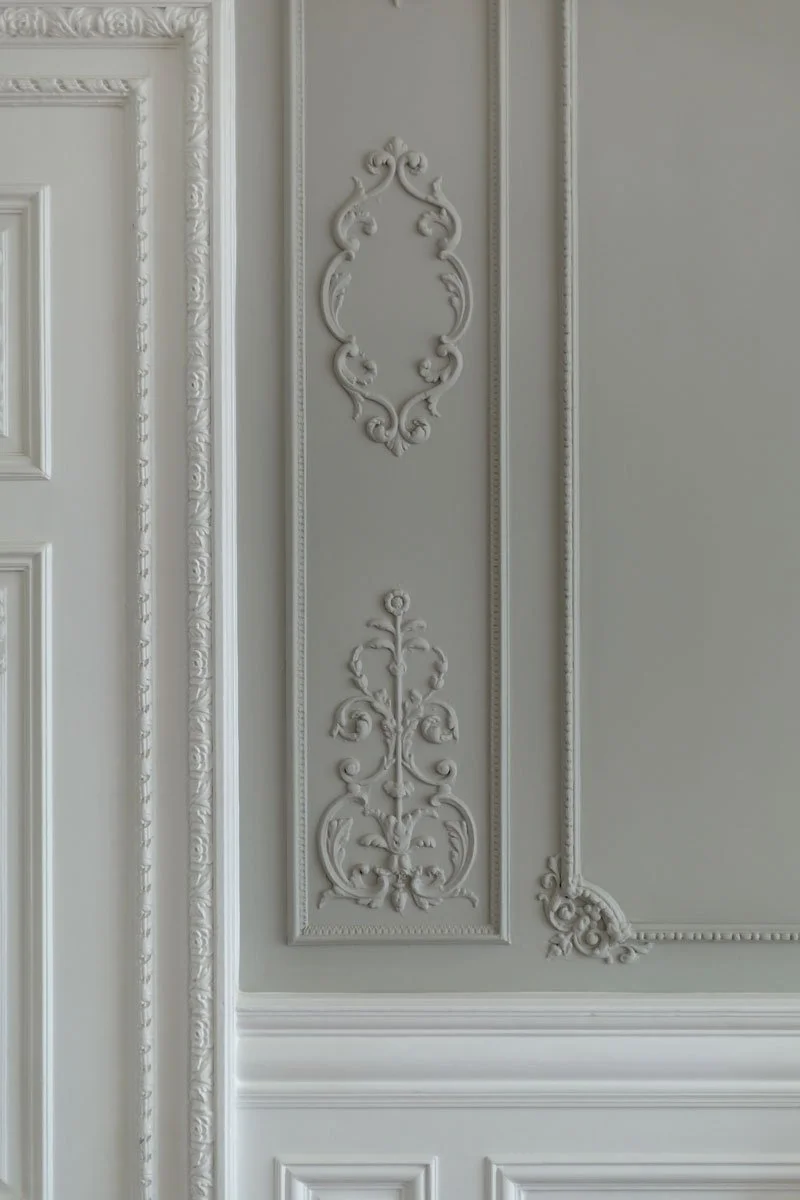 Close-up of ornate white decorative molding and trim on a wall and door in a classic interior.