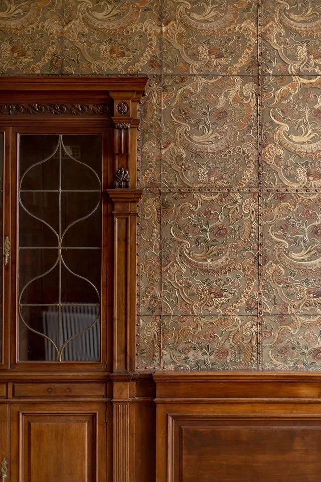 Wood-paneled wall with a glass-front cabinet on the left and ornate, patterned wallpaper behind.