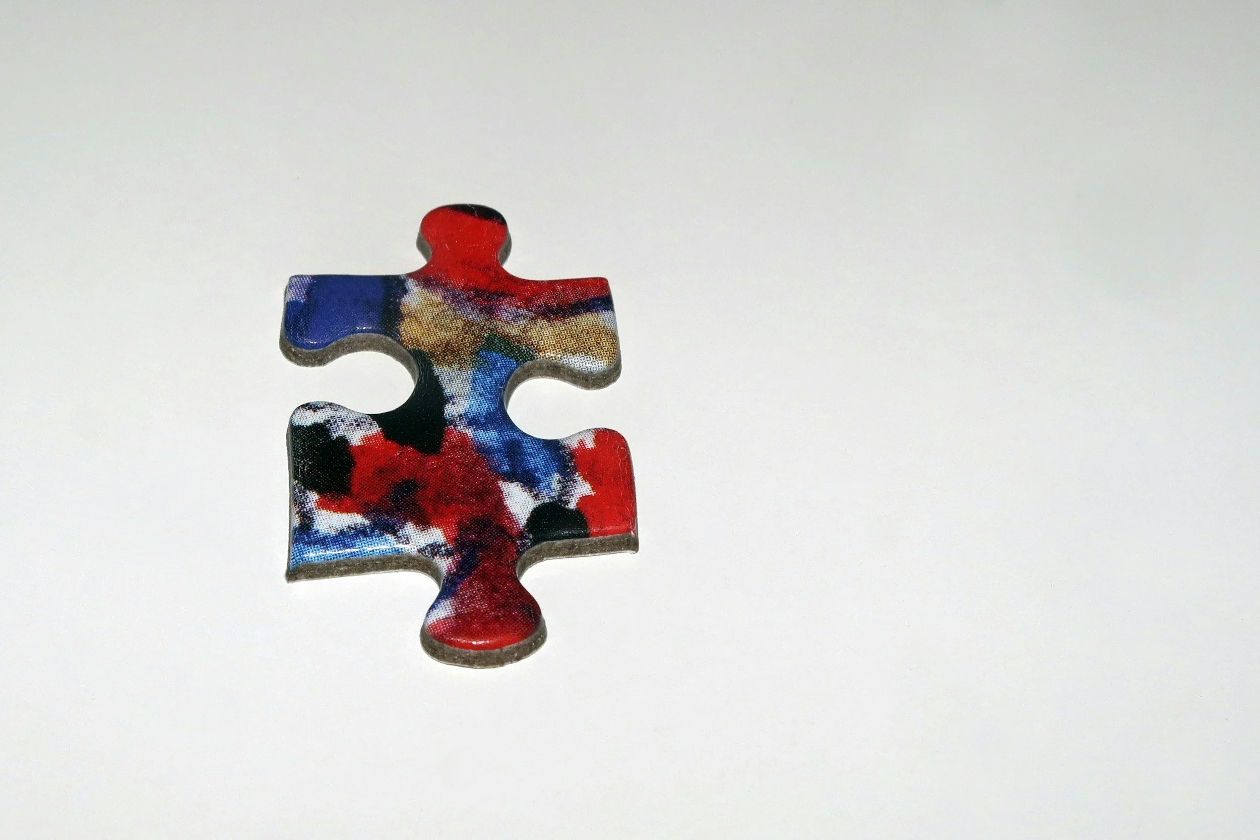 A puzzle piece with a colorful, abstract pattern, placed on a white surface.