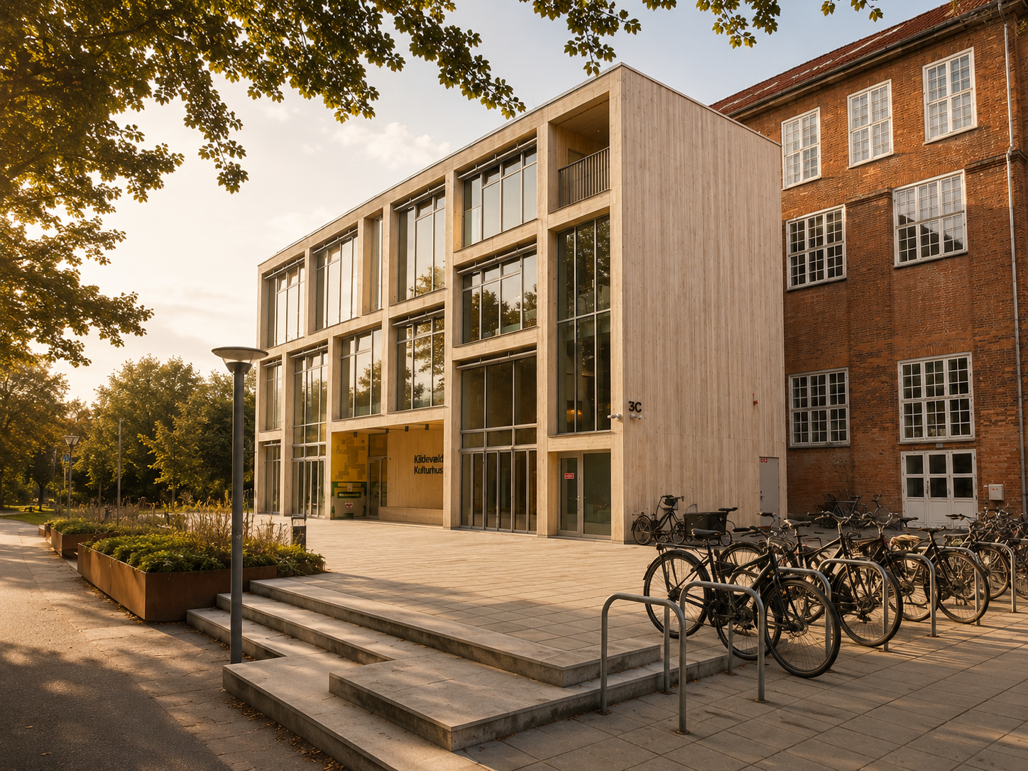Kulturel bygning med store vinduer og cykelparkering ude foran, omgivet af træer.
