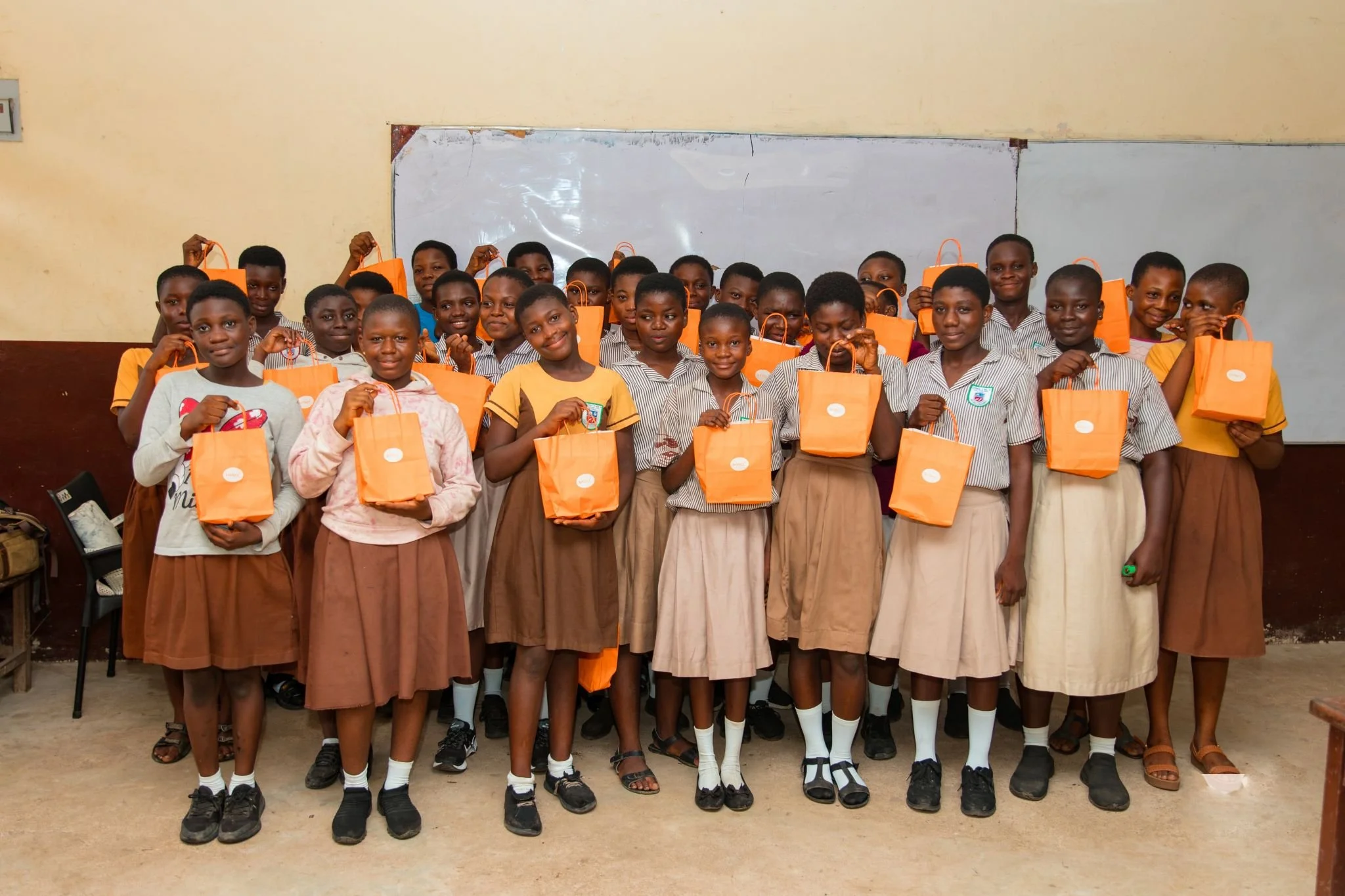 Group of school children holding orange gift bags inside a classroom.