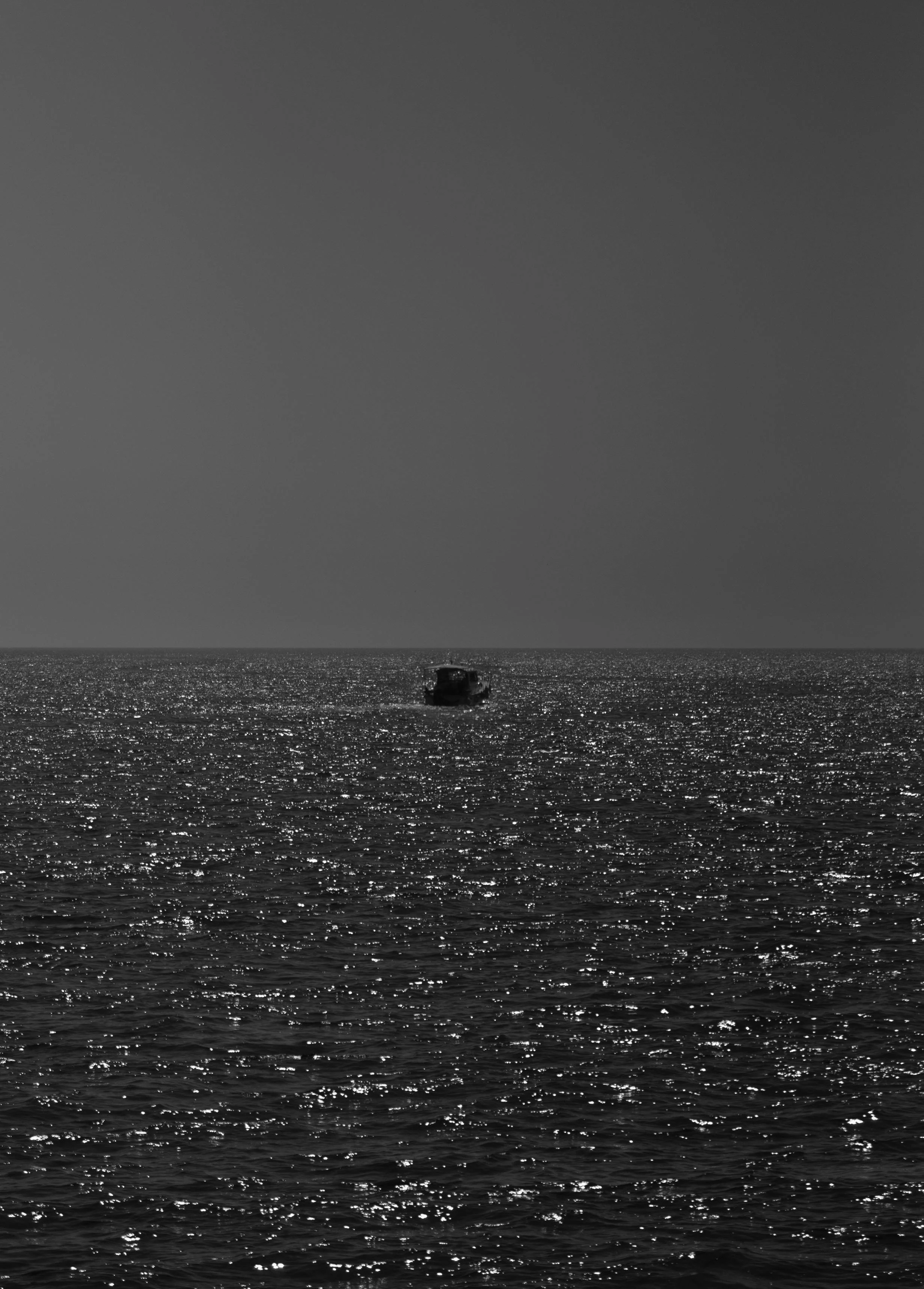 A boat floating on a shimmering ocean under a dark sky, with no other objects or landmarks visible.