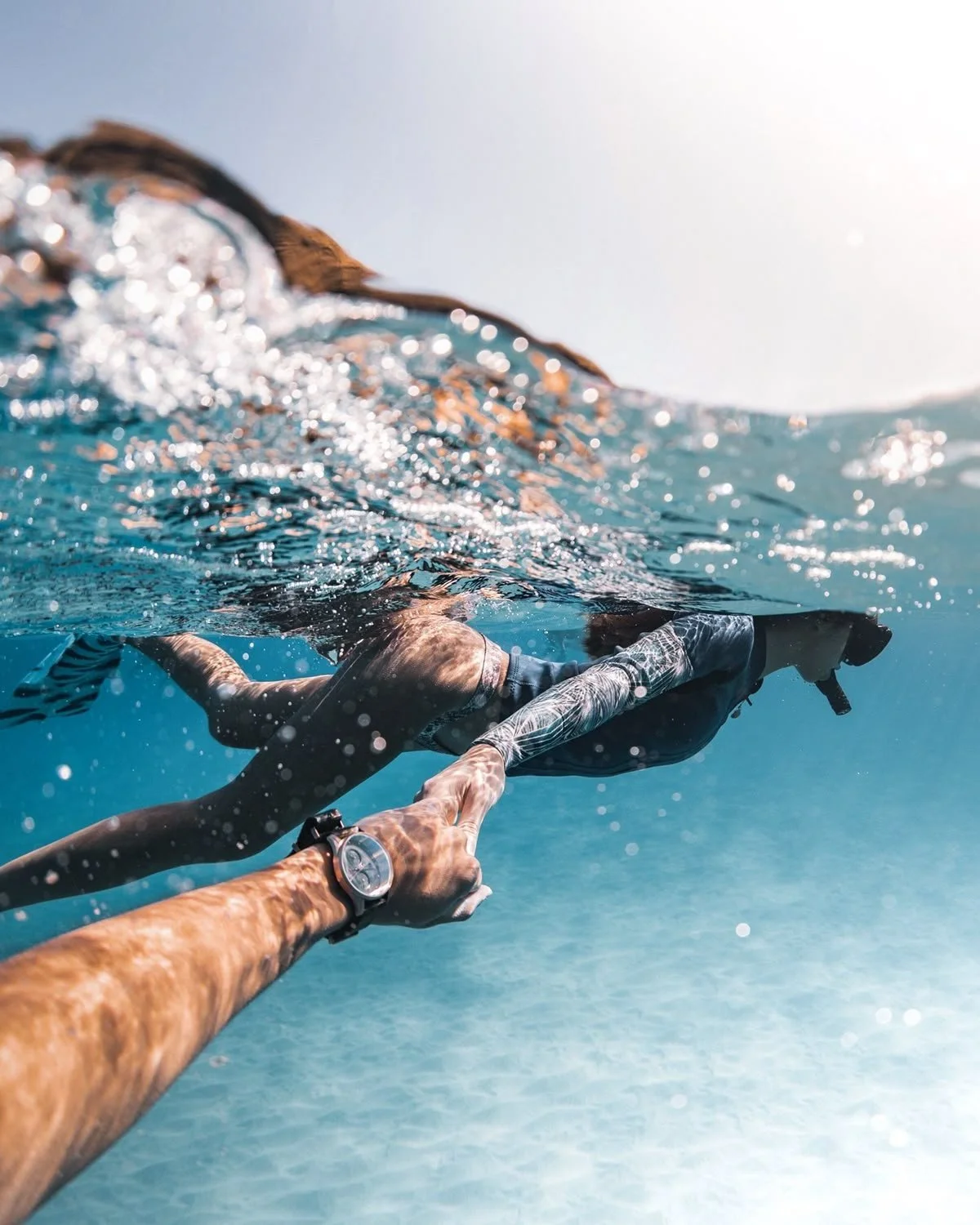 A person swimming in the ocean holding hands with another person above the water, with snorkel gear and swimwear.