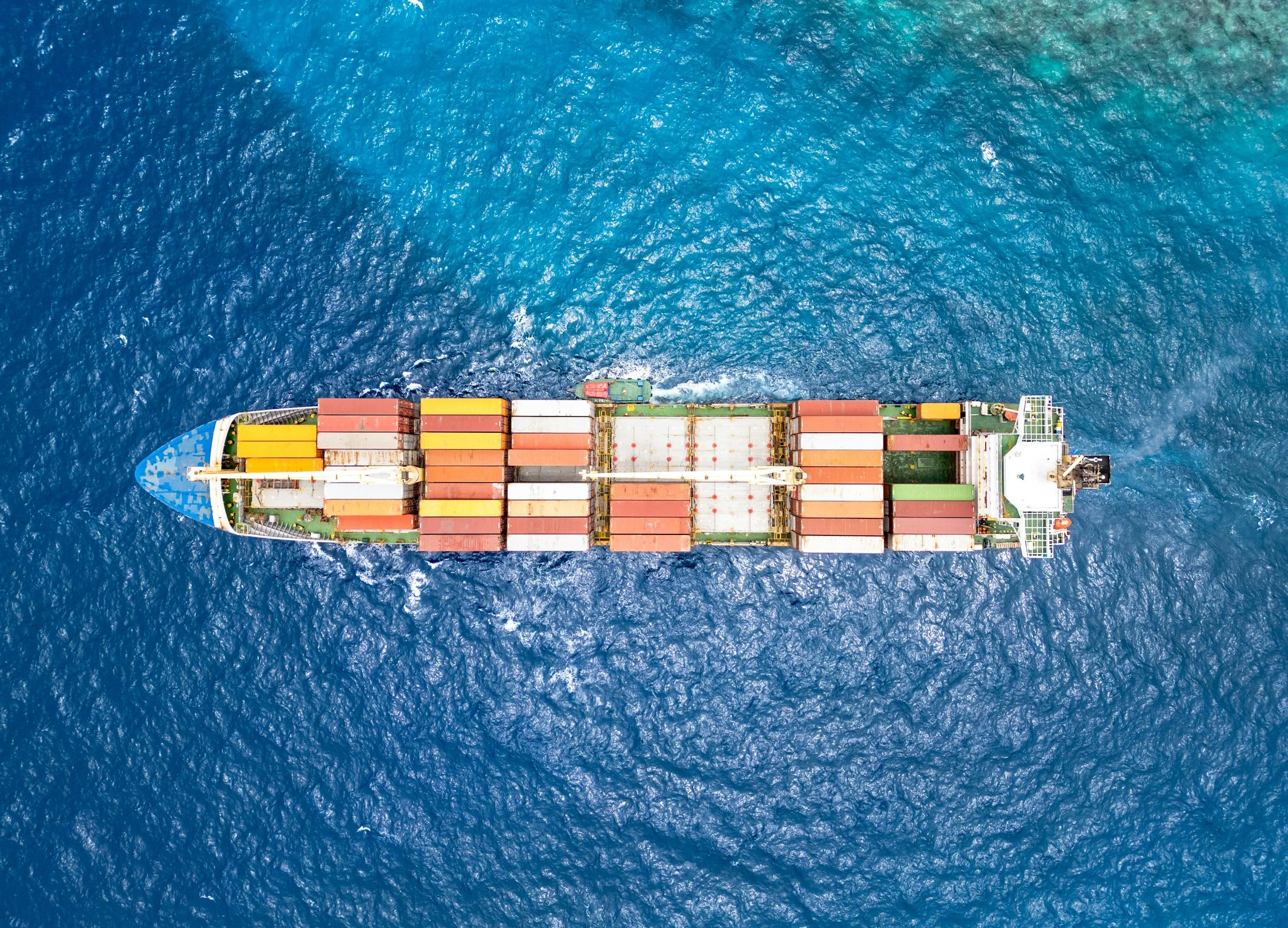 An aerial view of a large cargo ship in the ocean, carrying numerous multicolored shipping containers.