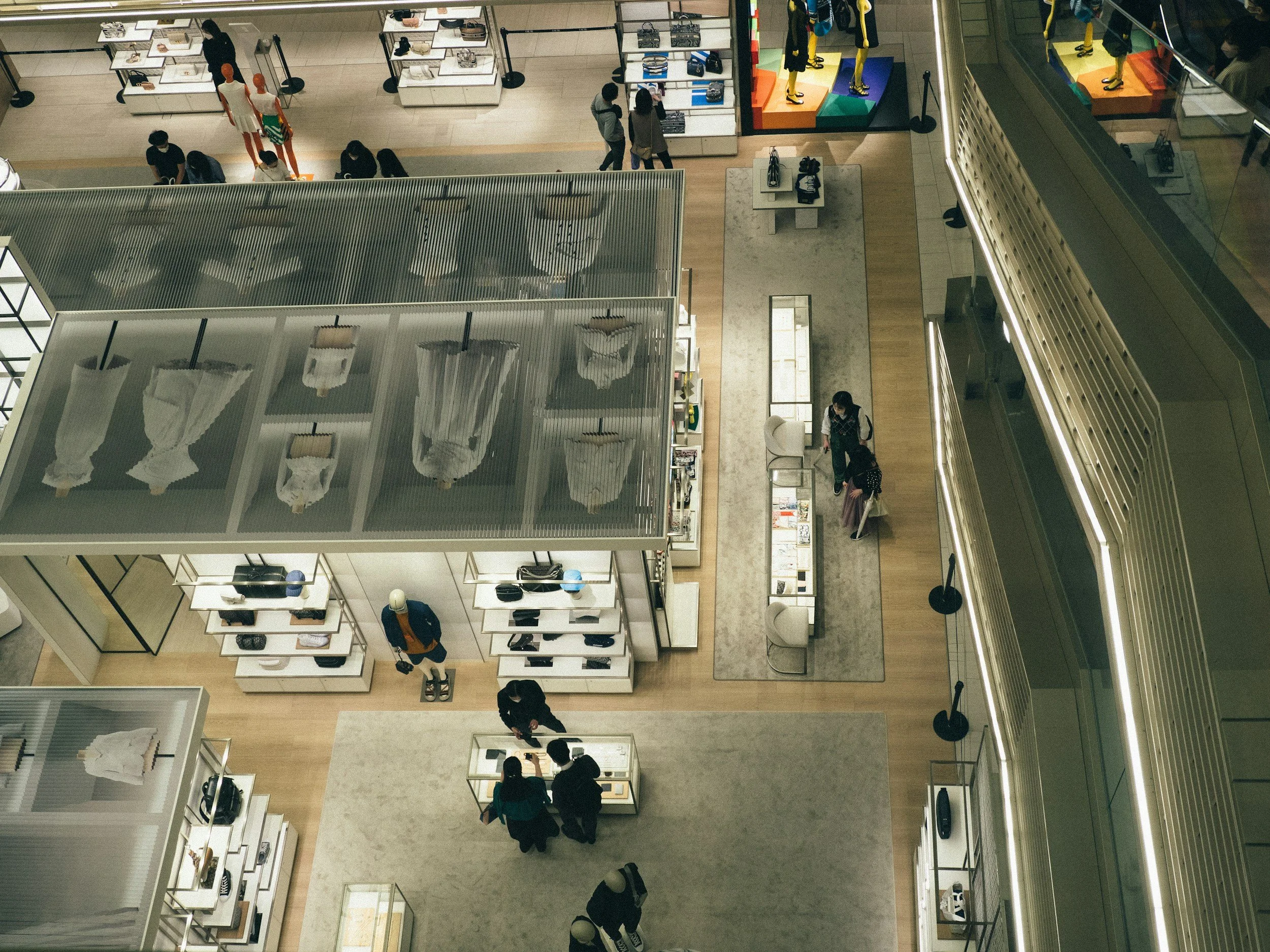 Aerial view of clothing and accessories displayed in a retail store within a shopping mall, with shoppers browsing and interacting with the displays.