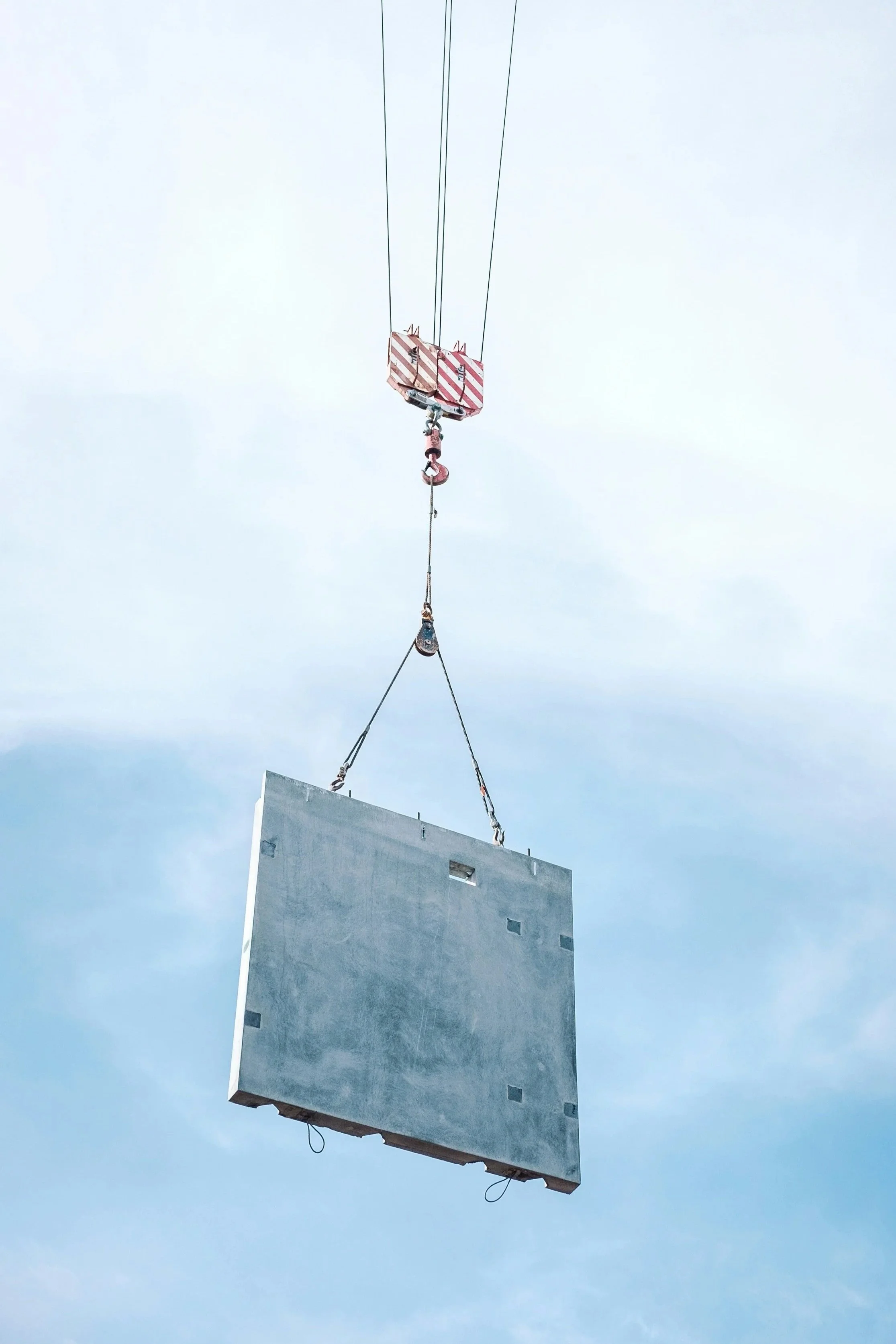 A large concrete panel is being lifted by a crane against a cloudy sky.