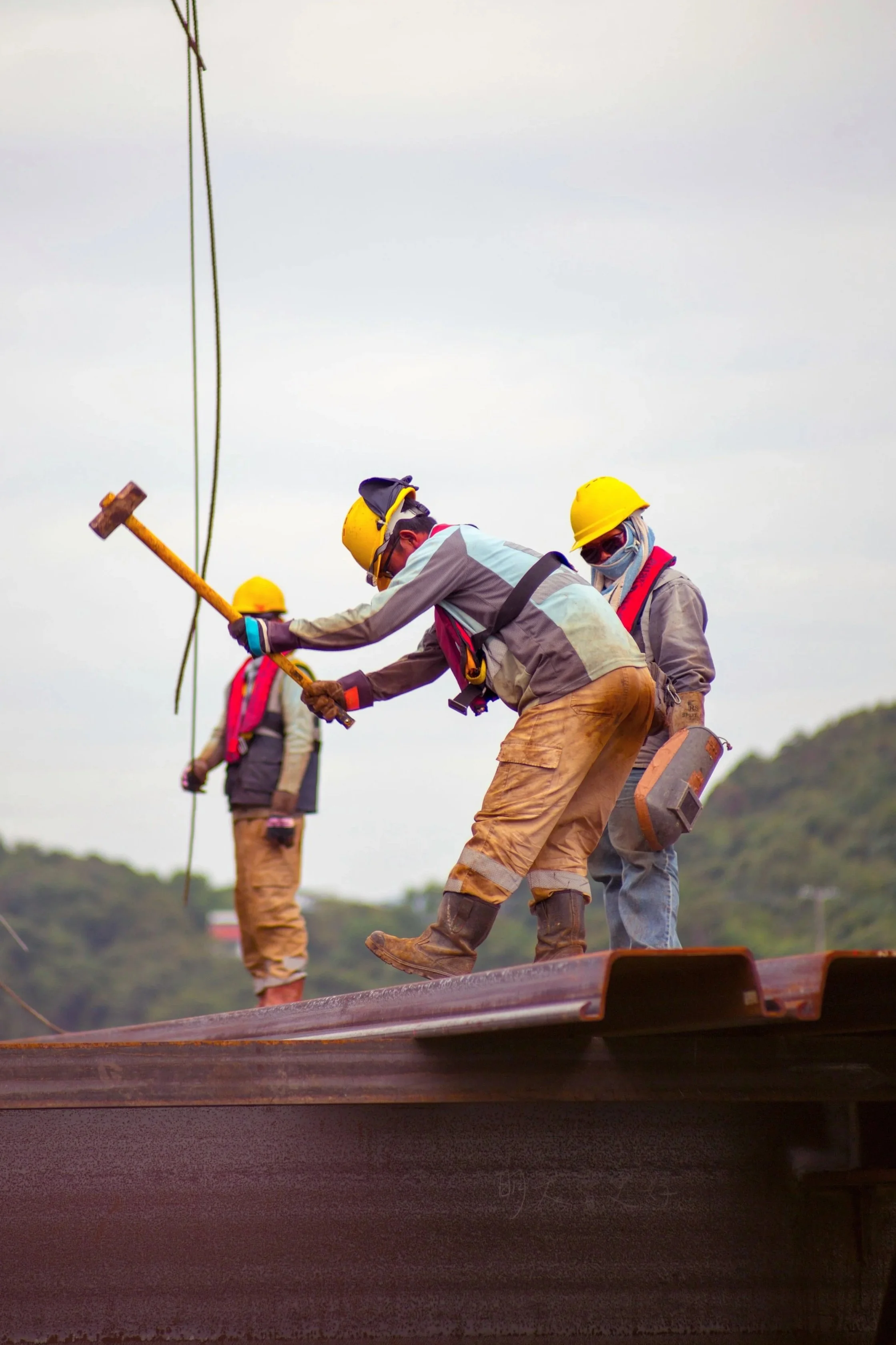 Construction workers wearing helmets and safety gear working on a metal structure outdoors.