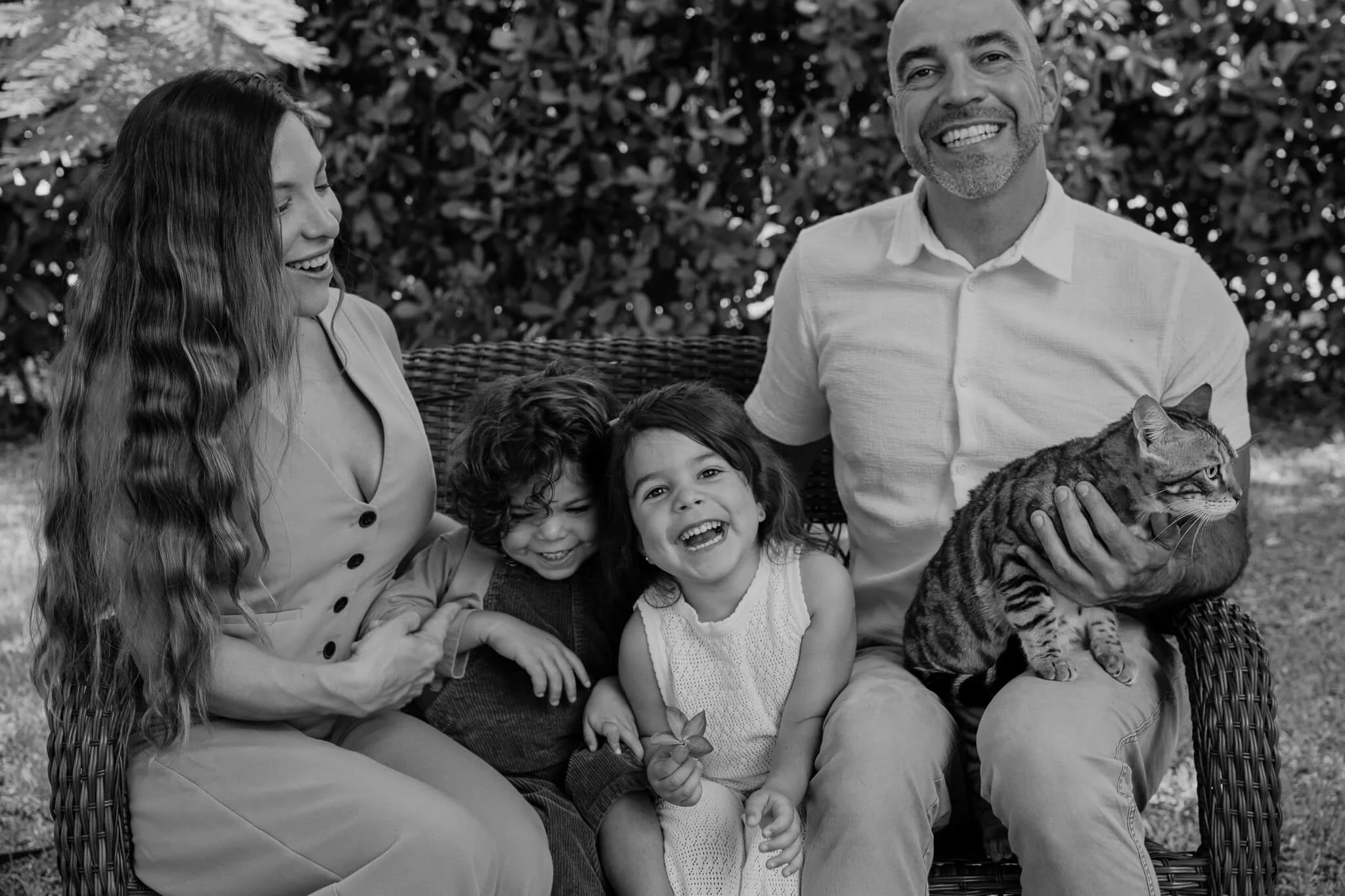 Grupo de personas y niños sonriendo con un gato en un entorno exterior.
