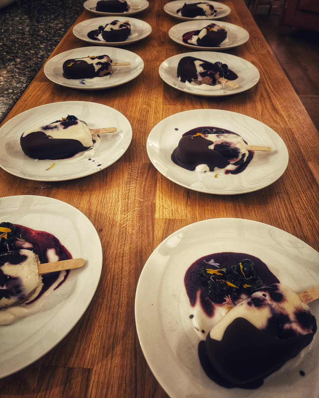 Multiple plates of blueberry popsicles with dark chocolate coating on a wooden table.