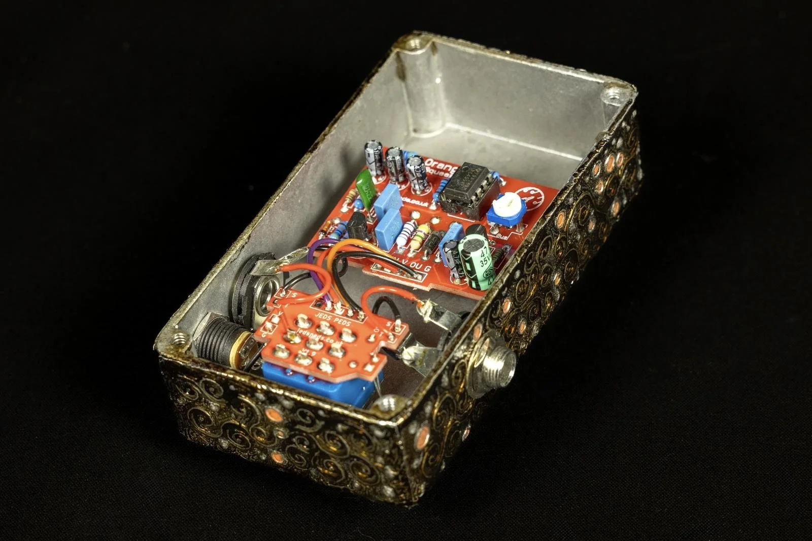 Inside of an electronic device with a metal case, revealing a red circuit board with various electronic components and some wires.