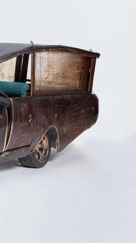Close-up of a vintage wooden car model with visible scratches and a single wheel on a plain white surface.