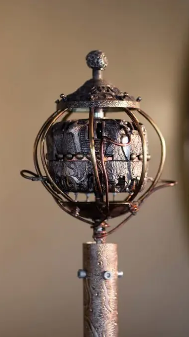 A steampunk-inspired device with a spherical metal cage topped by a textured finial, mounted on a wooden handle.