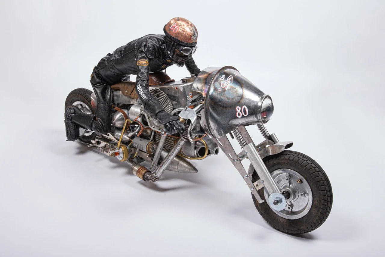 A model of a vintage motorcycle with a motorcyclist figure in black leather gear and helmet, positioned on a plain light gray background.