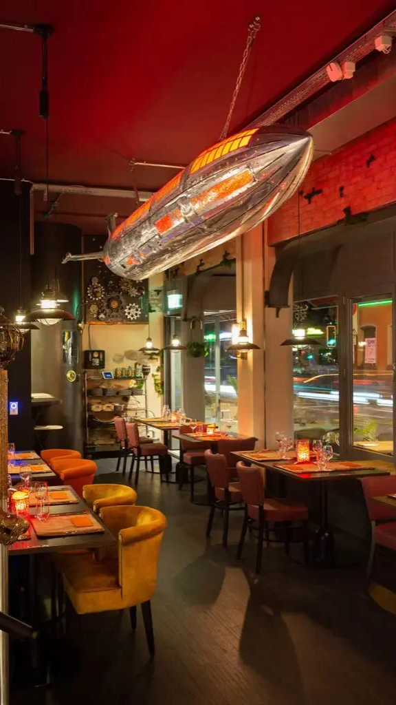 Interior of a restaurant decorated for Christmas with a hanging ziploc-shaped blimp or airship on the ceiling, tables set with glasses and candles, and large windows showing traffic outside.
