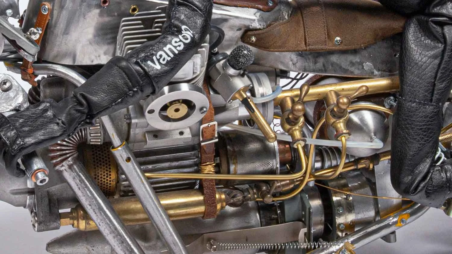 Close-up of a vintage aircraft engine with various metallic parts, tubes, and leather gloves.