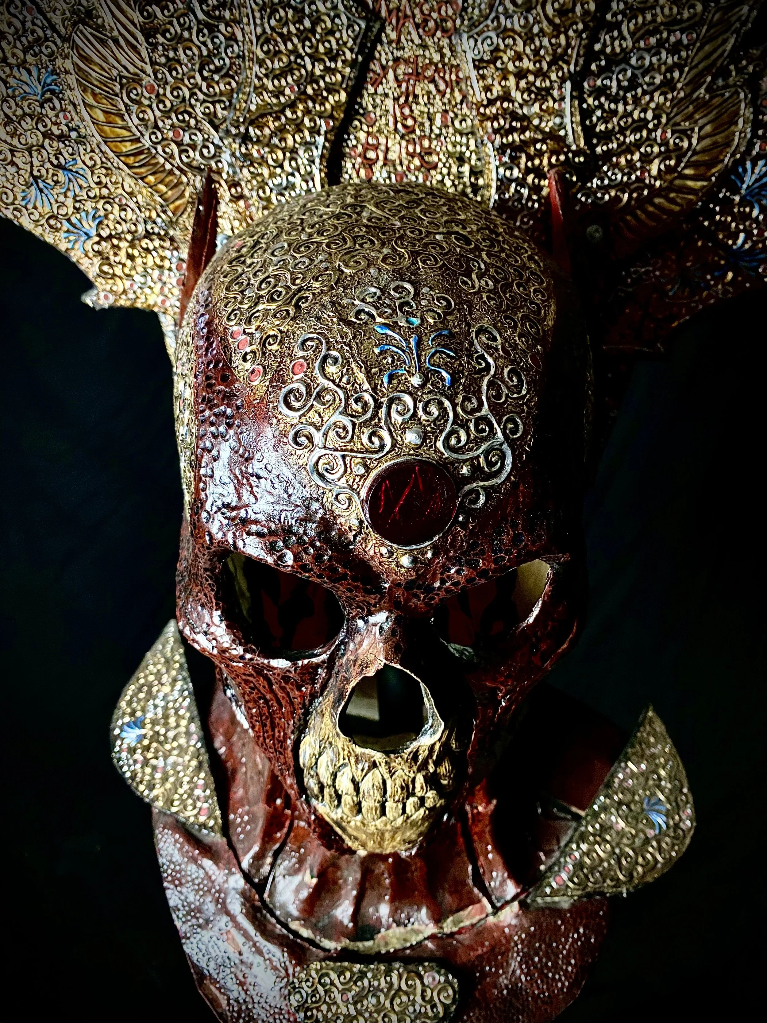 Ornate skull with intricate gold and red detailing, surrounded by decorated adornments and elaborate patterns.