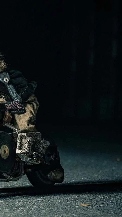 Close-up of a small, remote-controlled car with a rough, weathered appearance, on a dark asphalt surface.
