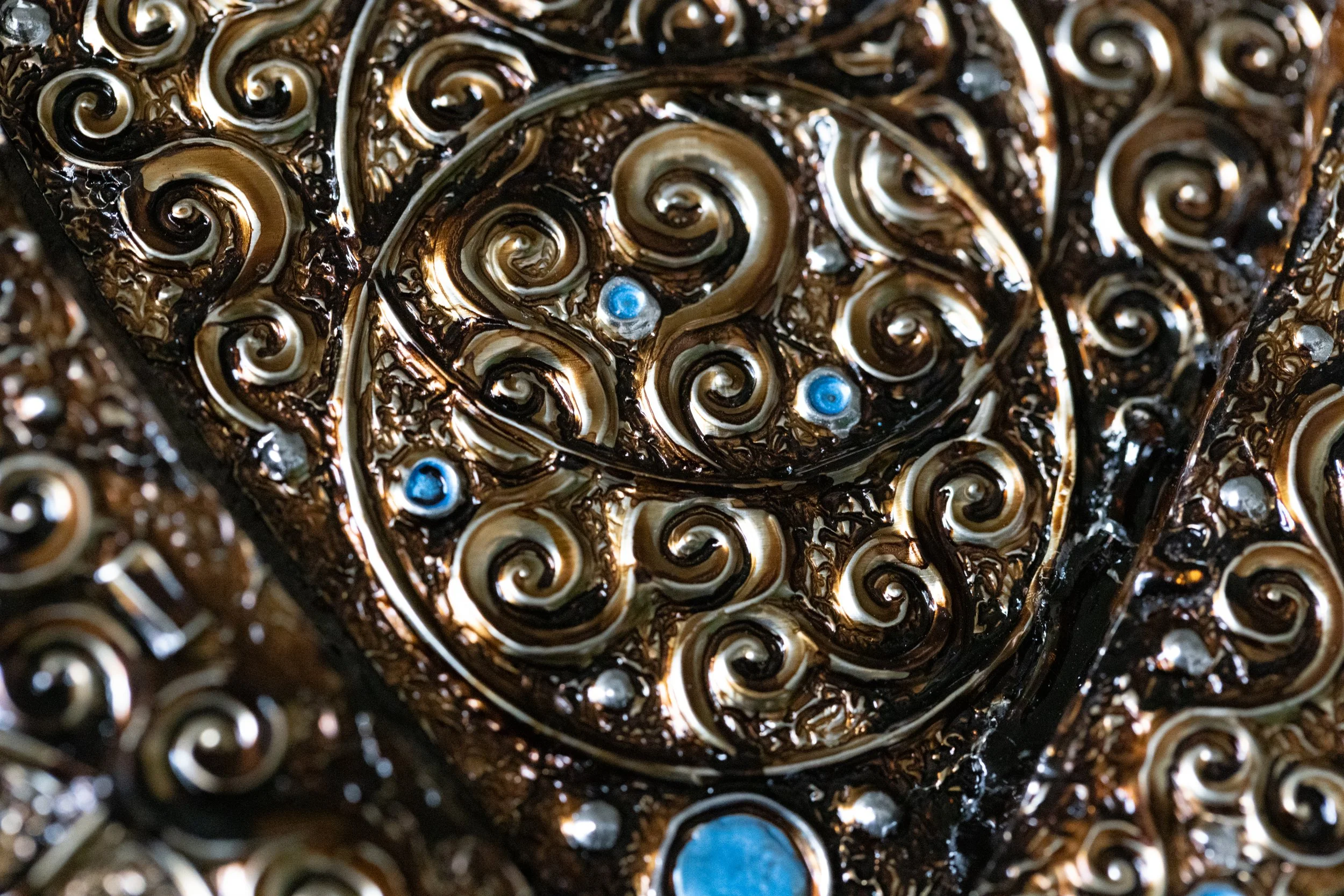 Close-up of an ornate metal artifact with intricate swirling patterns and embedded blue stones.