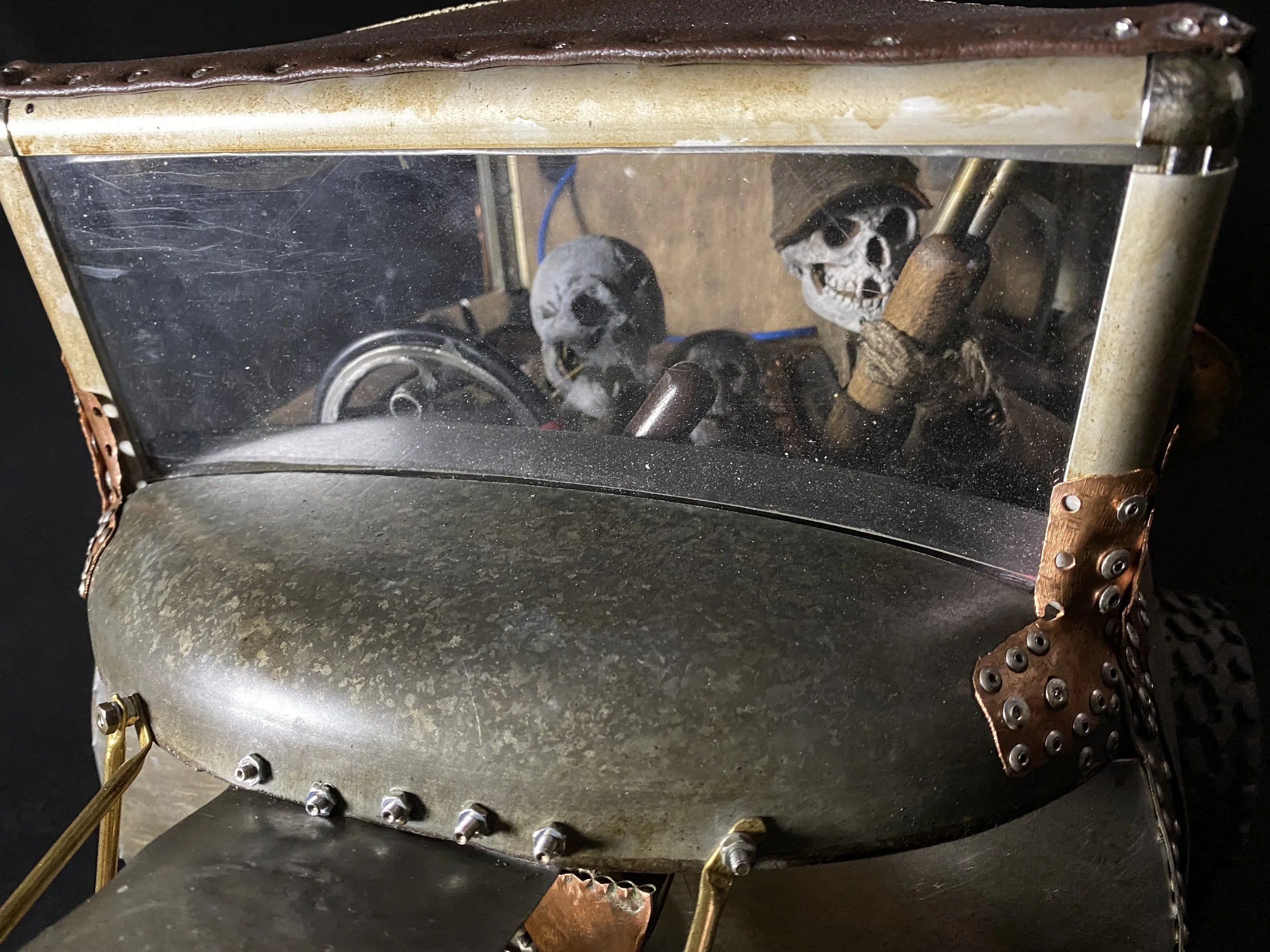 A miniature vintage race car with a clear windshield, containing small skull decorations in place of a driver.