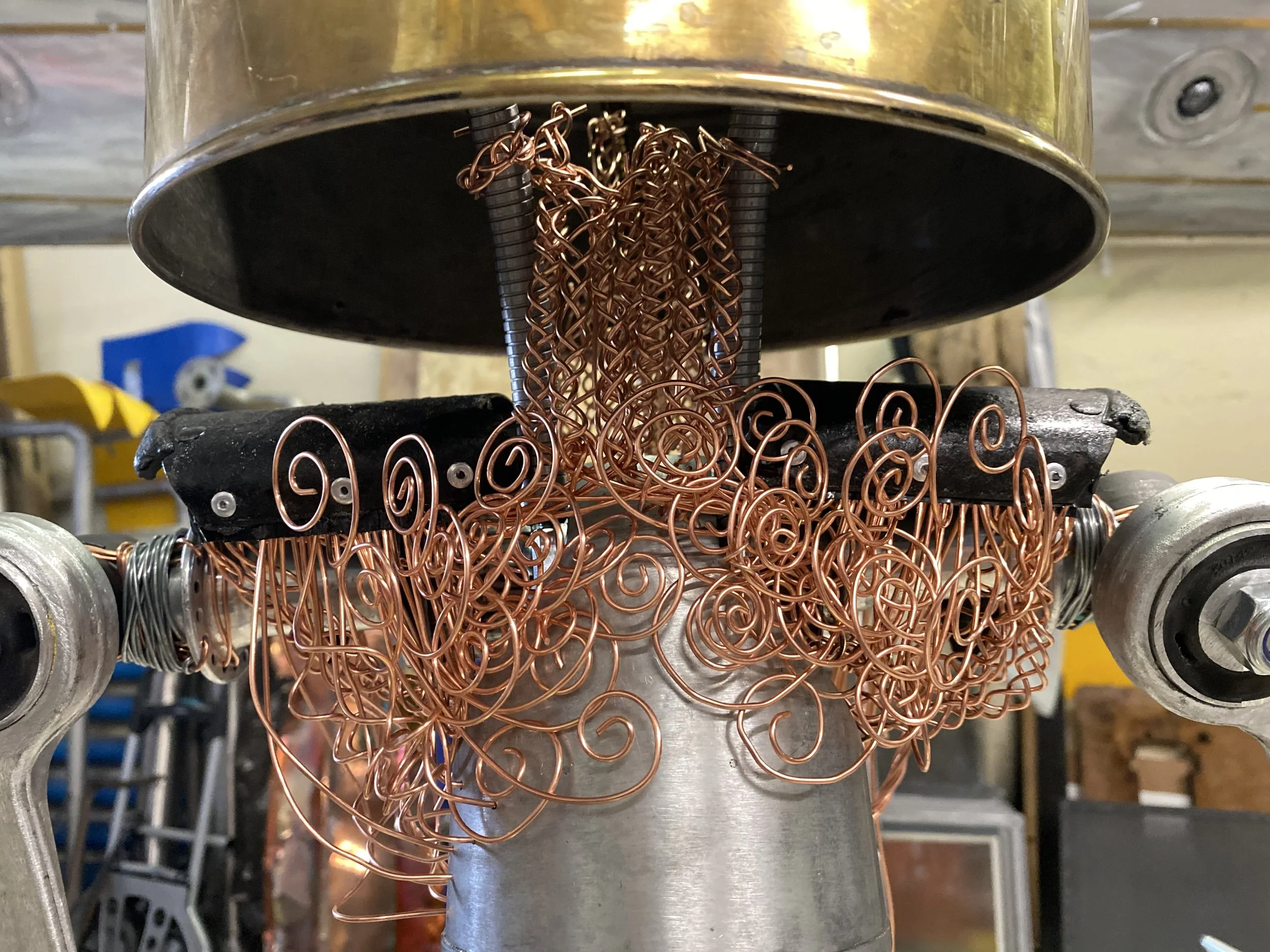 A machine designed to wind copper wire with metal guides and rollers, working with a coiled copper wire still in process.