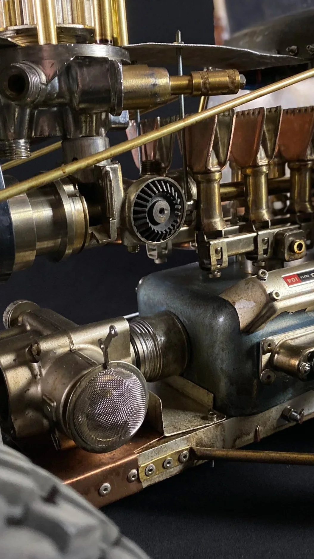 Close-up of a vintage steam engine with metallic components, including pipes, gears, and valves, set against a dark background.
