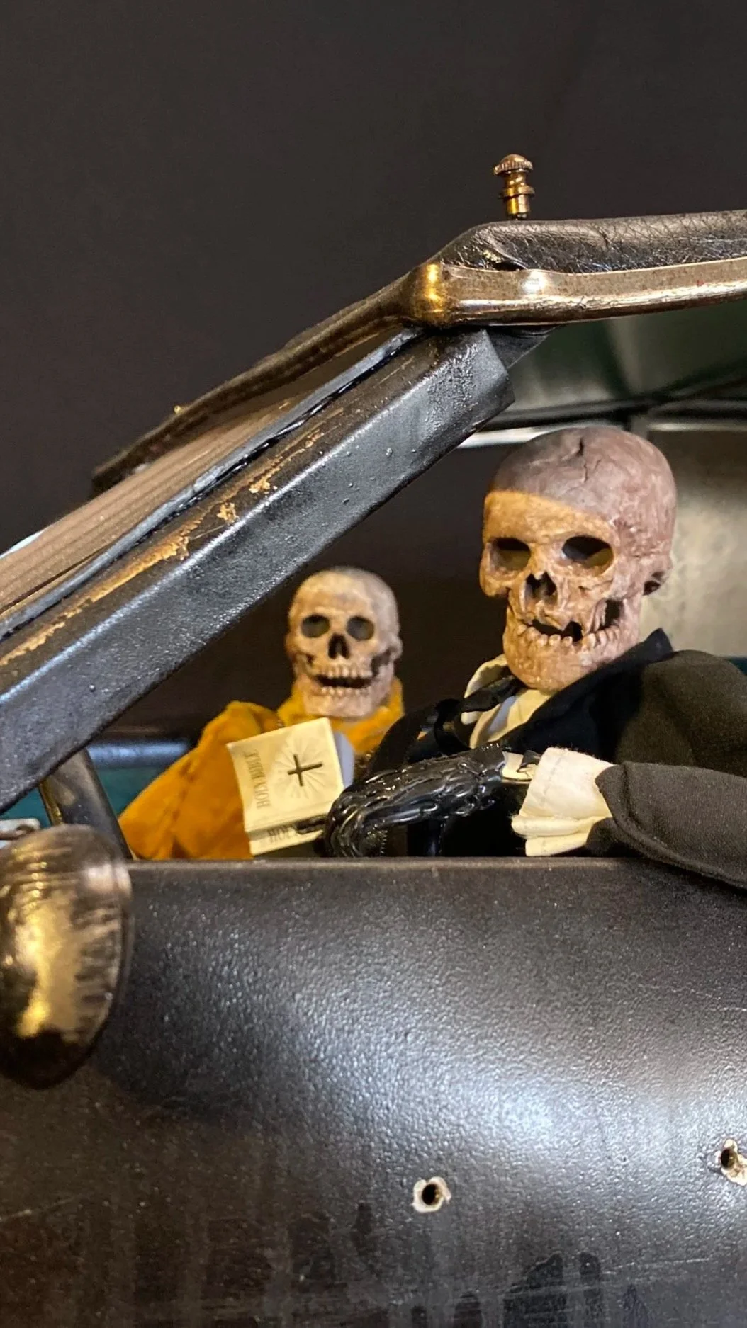 Two skull decorations with skeleton faces, dressed in black and orange clothing, placed on a black surface with a black background.