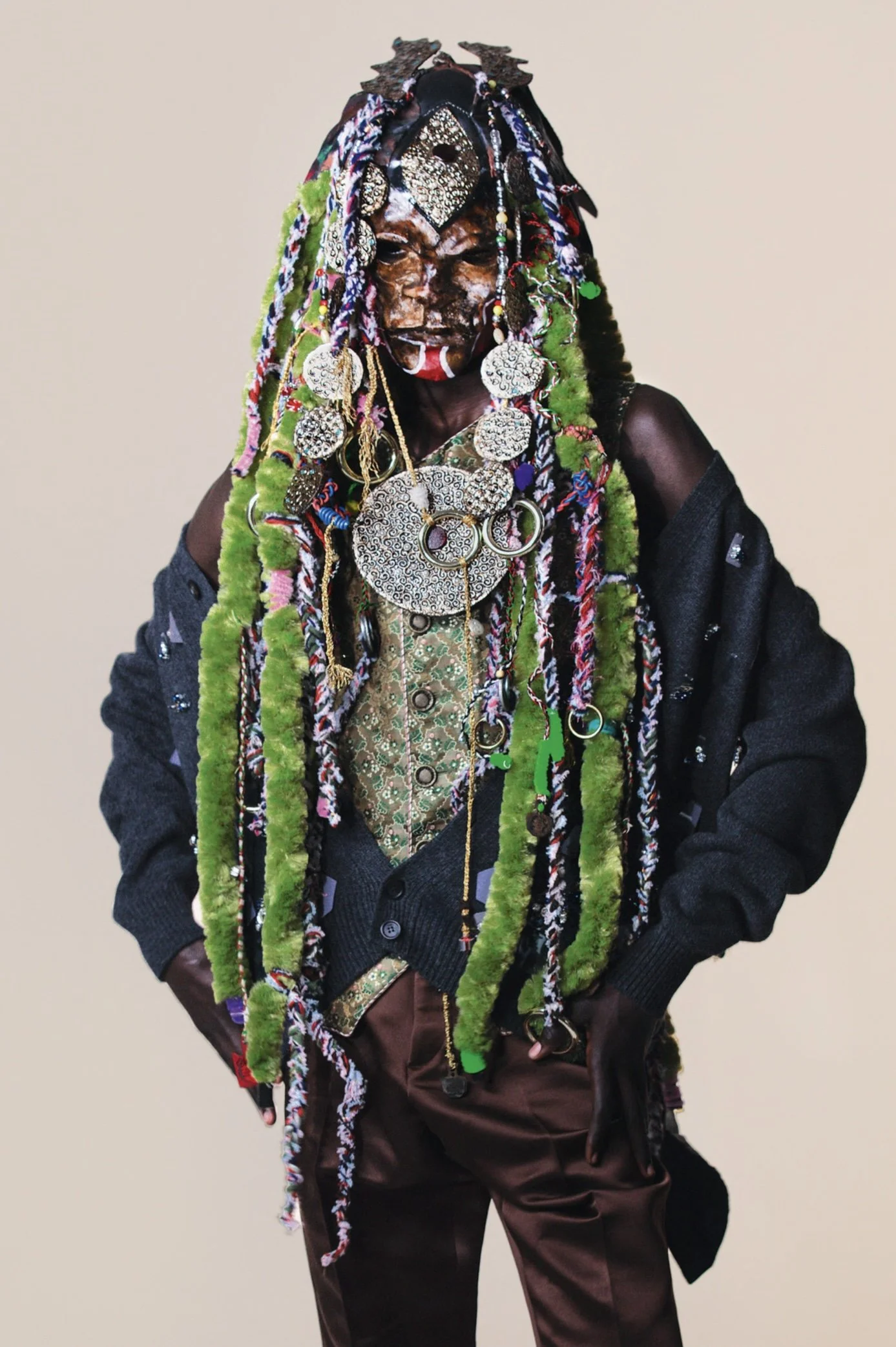 A person in colorful, elaborate clothing with long, multicolored dreadlocks, wearing extensive jewelry and face paint.