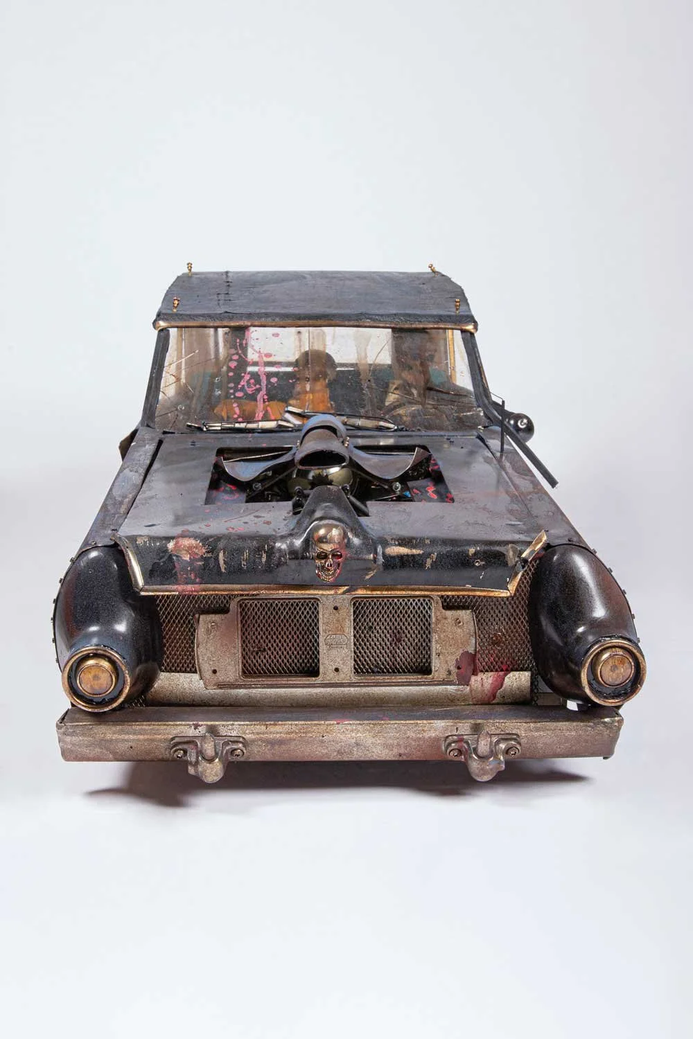 A model or replica of a vintage, weathered car with a skull decal on the front, a large-propelled engine protruding from the hood, and a worn, scratched exterior with a dark, possibly bloodstained, finish.