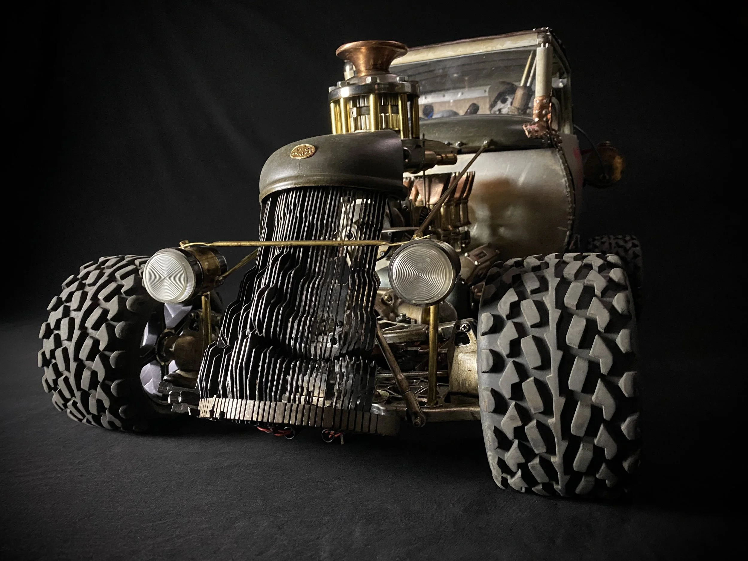 A vintage-style remote-controlled toy car with large off-road tires, an exposed engine, and a minimalistic metal and brass body, set against a black background.